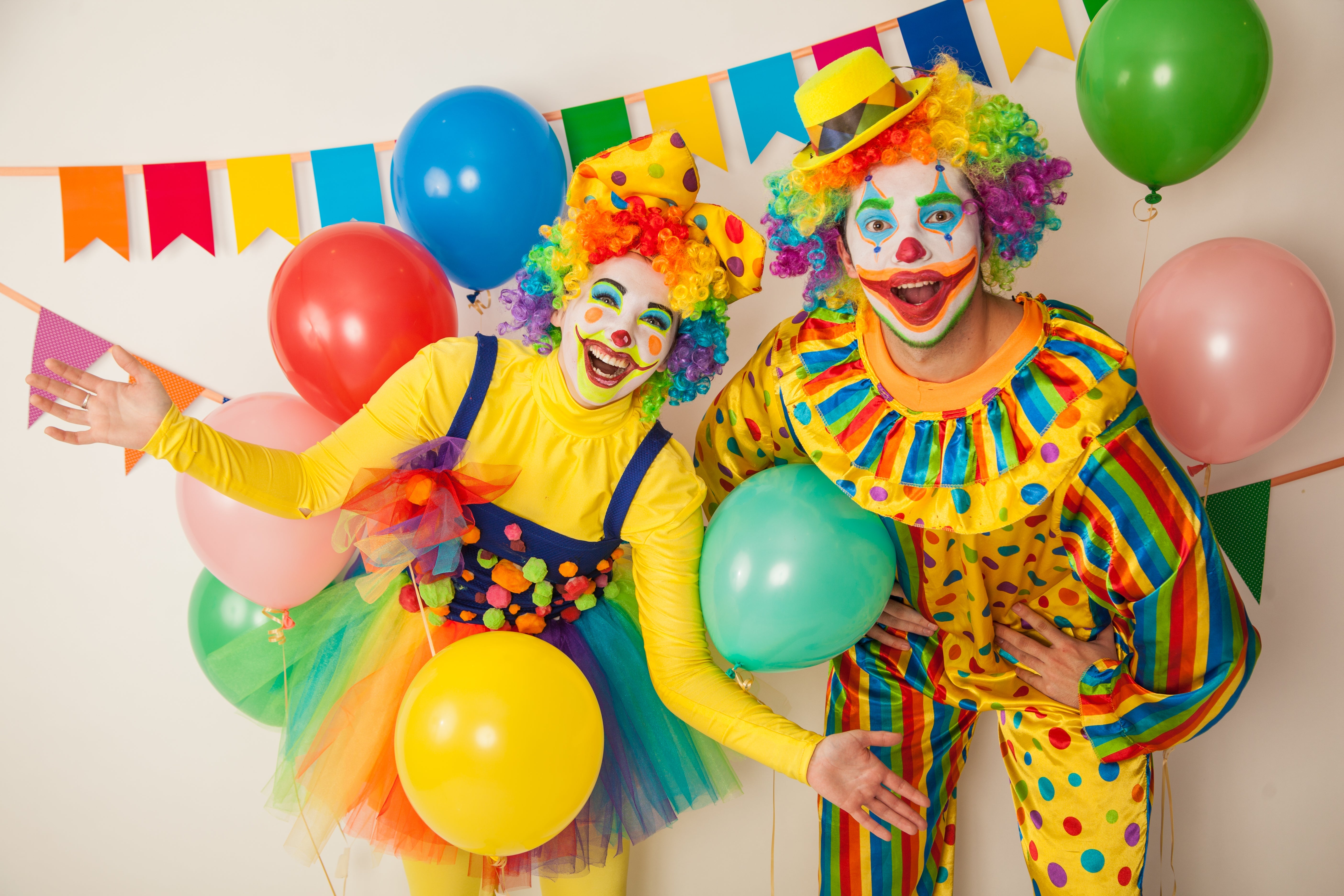 A vibrant collection of friendly circus and clown fancy dress costumes, featuring a smiling clown in a colorful polka-dot suit with a rainbow wig, alongside a ringmaster wearing a bright red tailcoat and top hat.