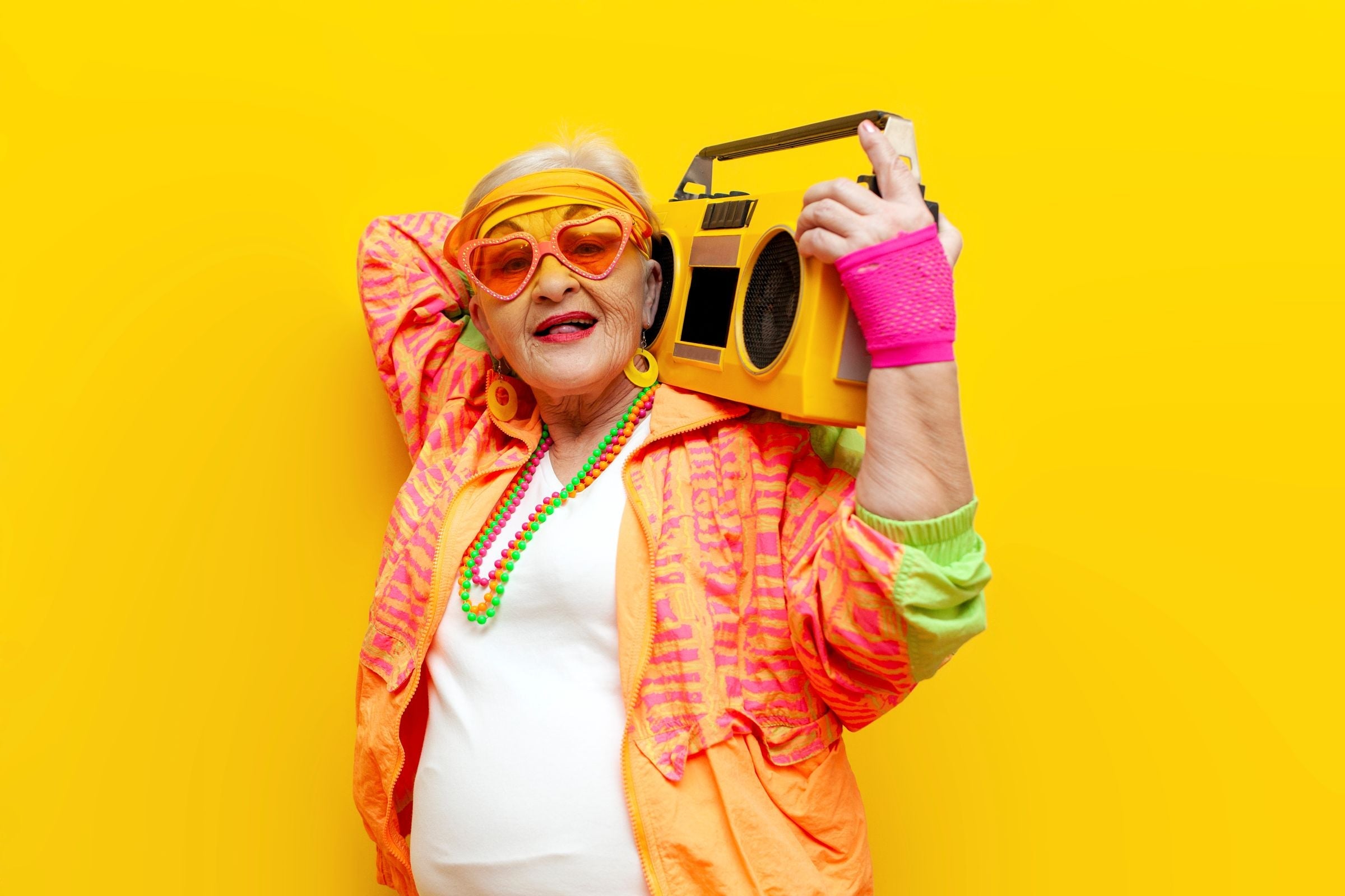 A old woman with boombox wearing collection of bright neon 1980's accessories including pink mesh gloves, and multi-coloured bead necklaces.