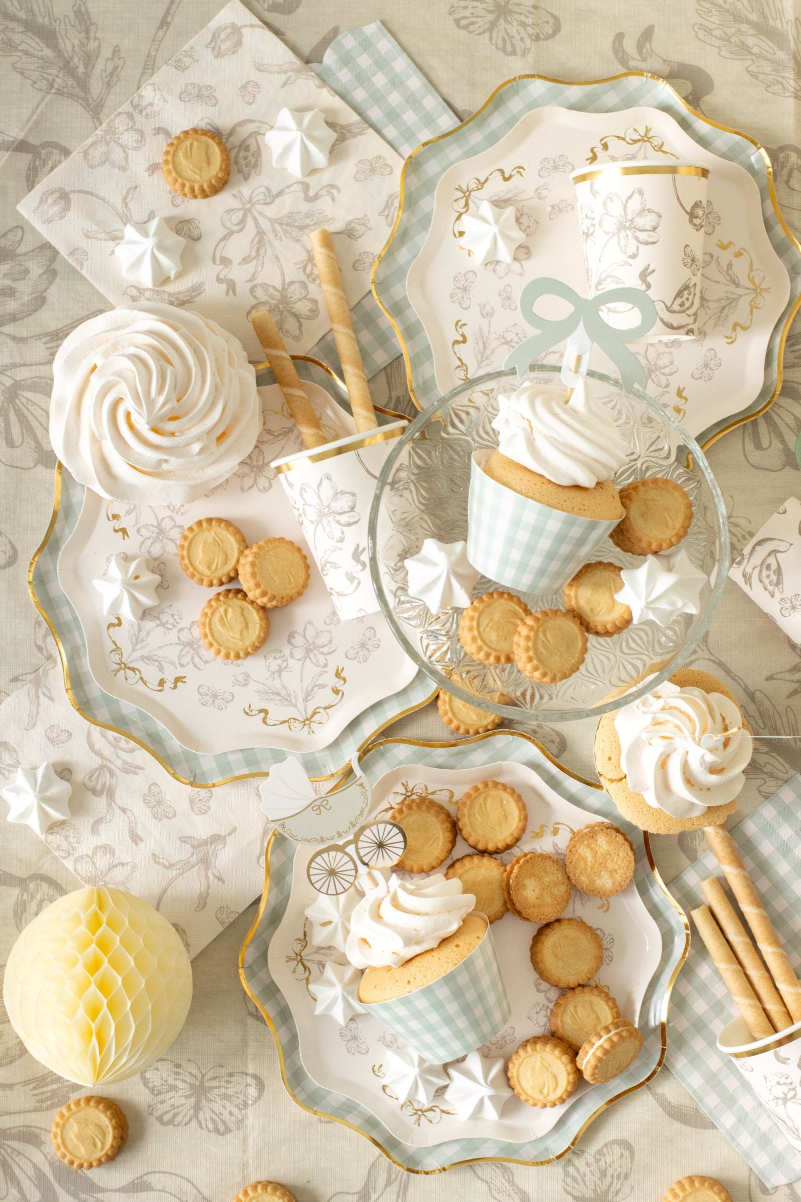 Overhead view of a party table featuring beige floral napkins, matching plates, and gold-edged cups.