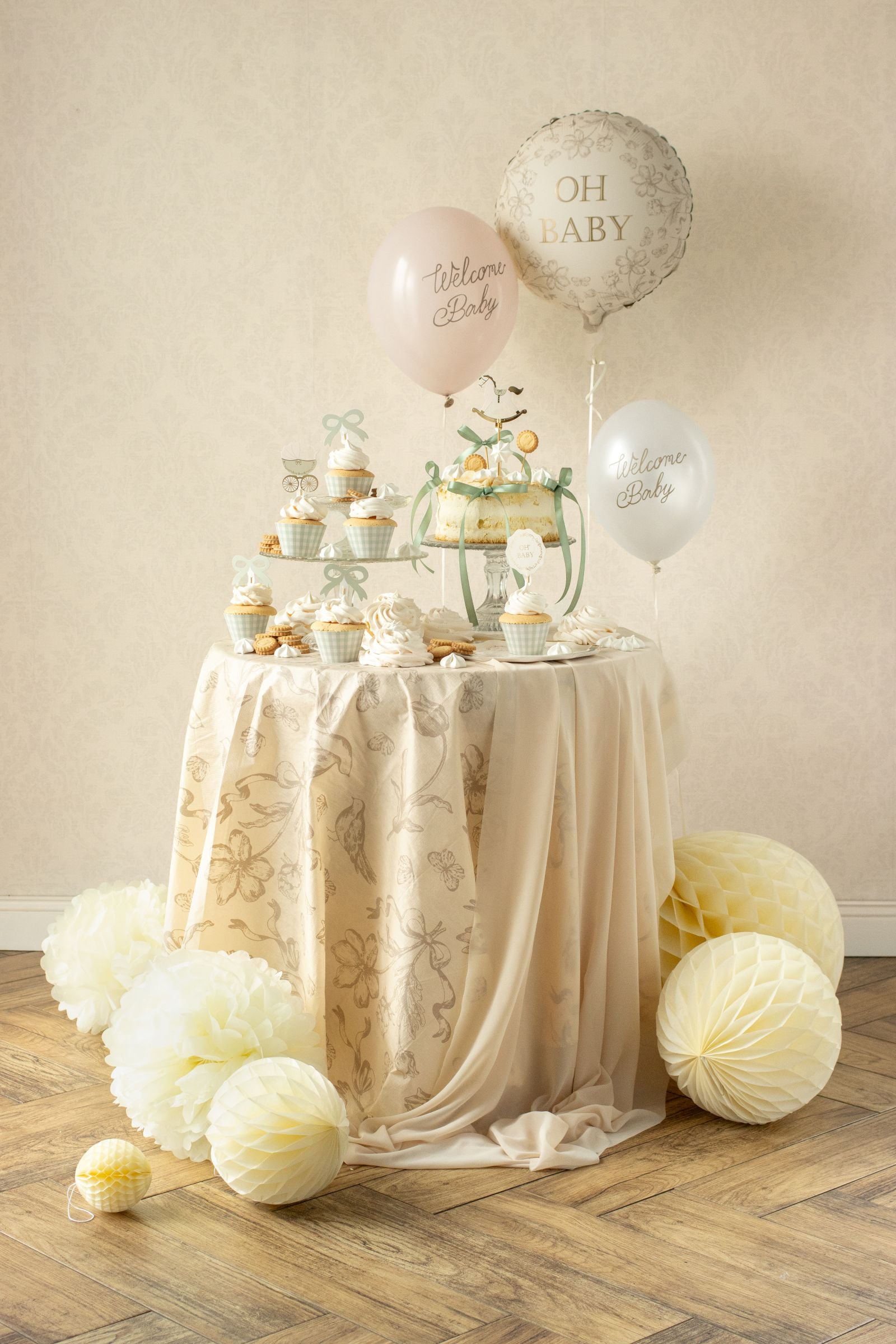 Party table covered with a beige floral tablecloth next to honeycombs and baby balloons.