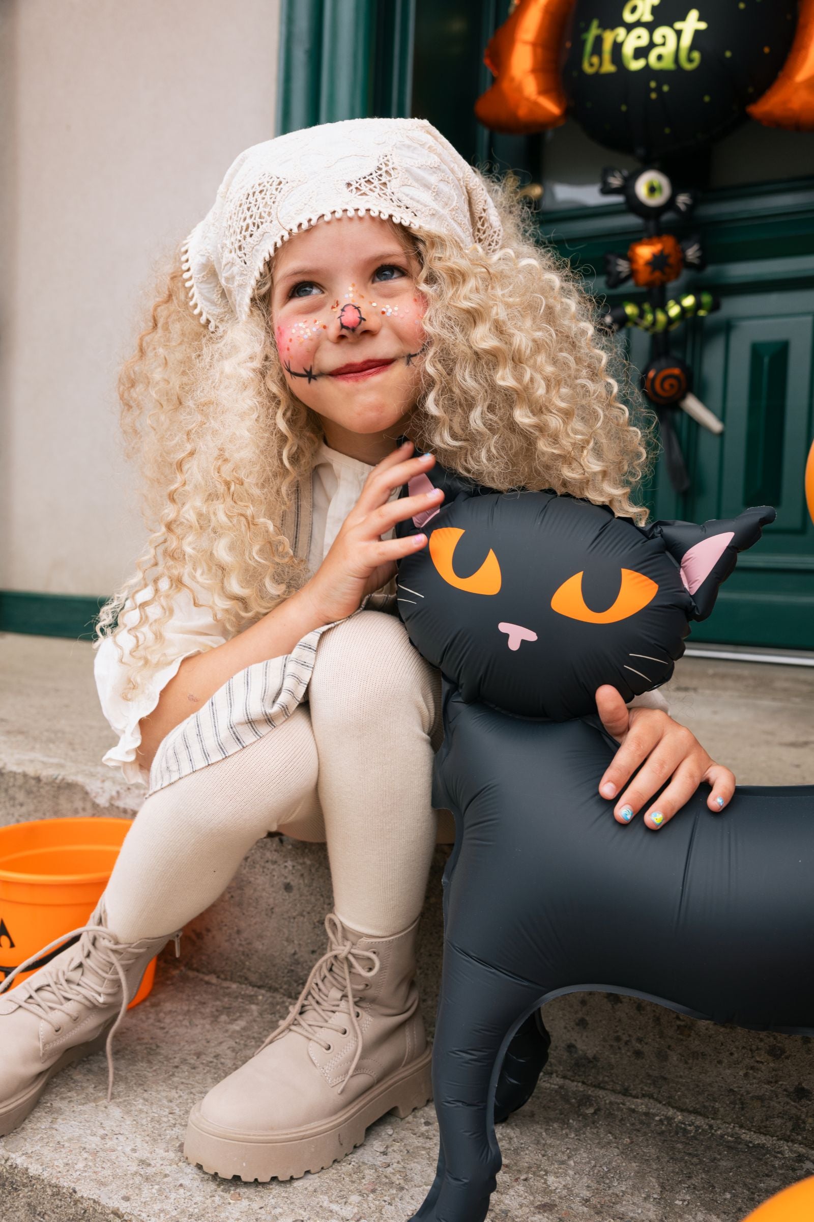 Close-up of a smiling young girl in a Halloween costume holding the matte black cat standing foil balloon.