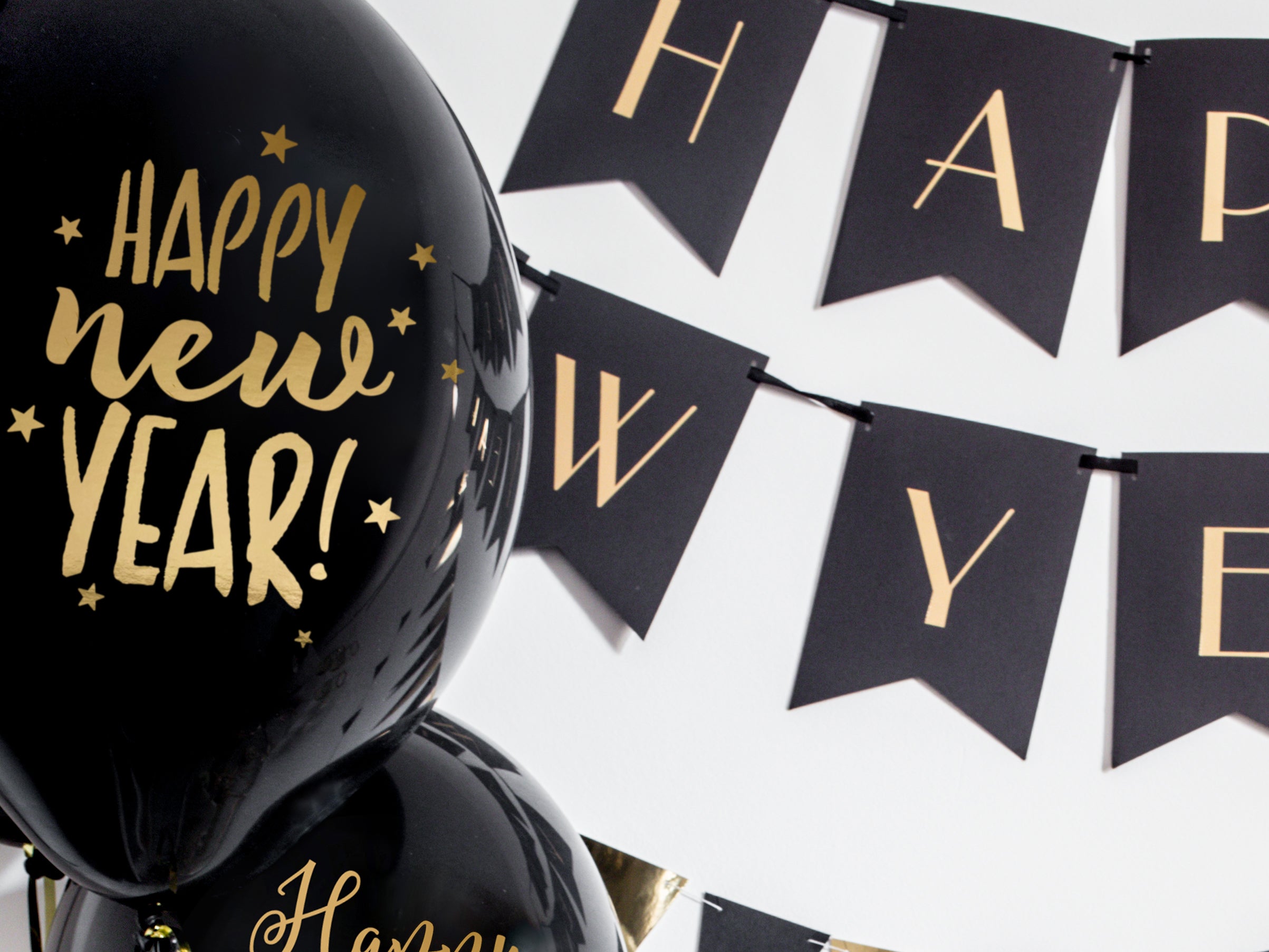 Black and gold Happy New Year party decorations featuring balloons and a matching letter banner.