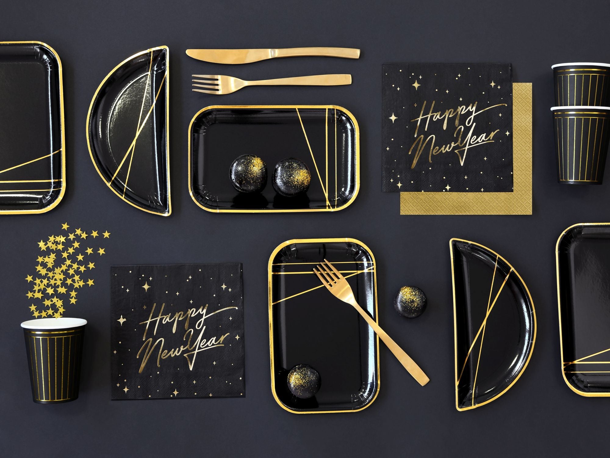 Luxury NYE party supplies including black and gold plates, cups, and Happy New Year napkins.