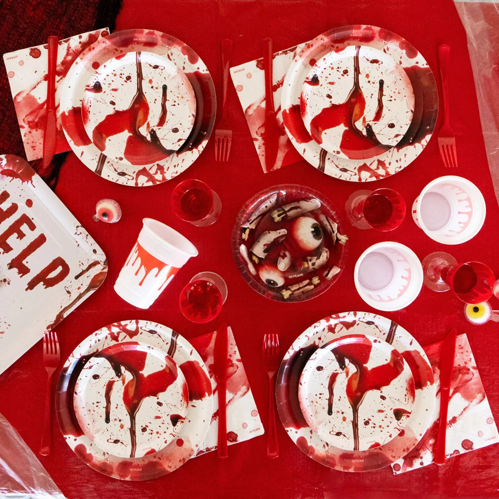 Top-down view of a Halloween party table featuring a red tablecloth set with blood-splatter plates, red cups, and a central snack bowl decorated with a severed body parts design.