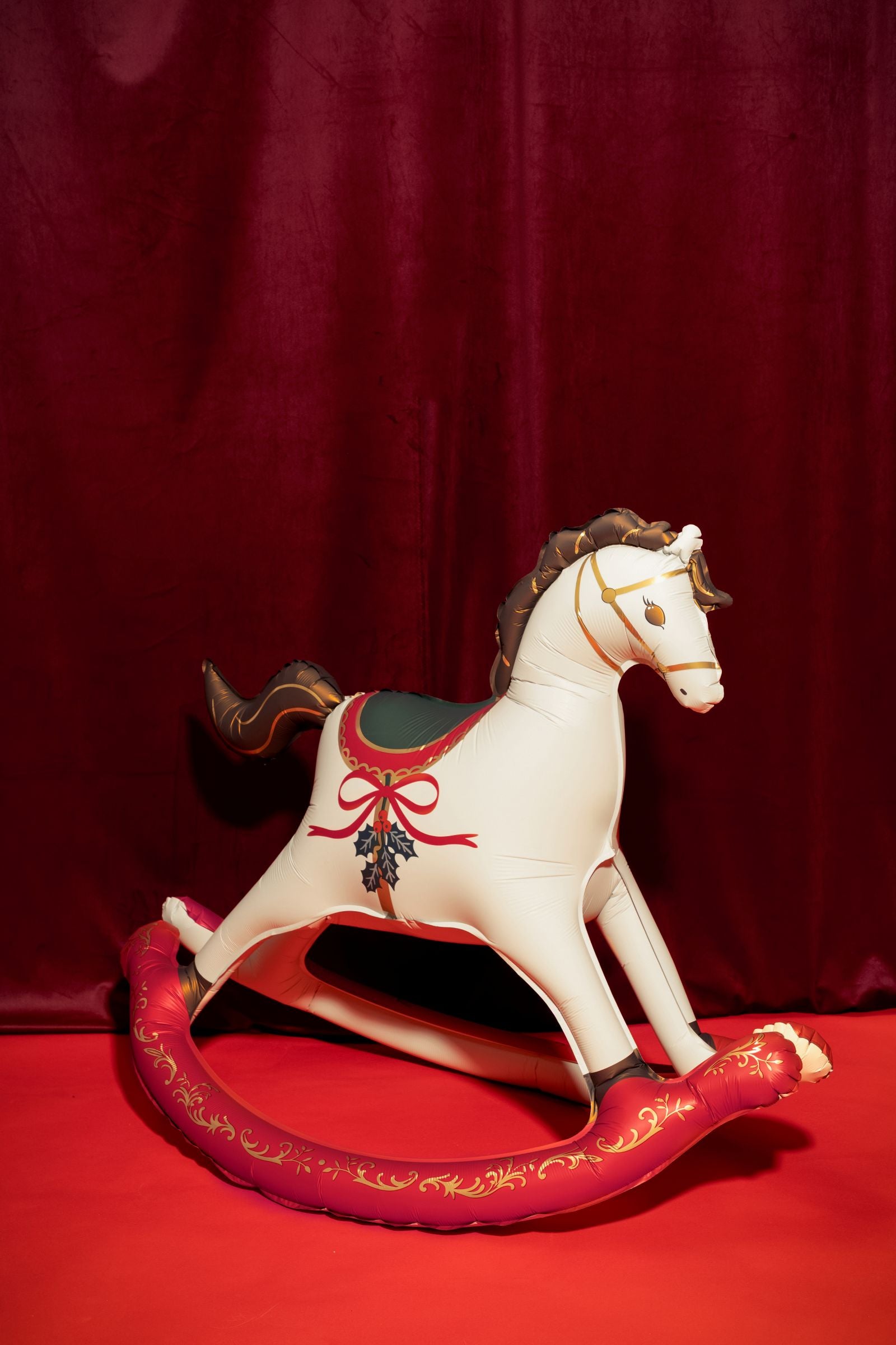 The inflatable Christmas rocking horse sitting on a red floor against a dark velvet background.