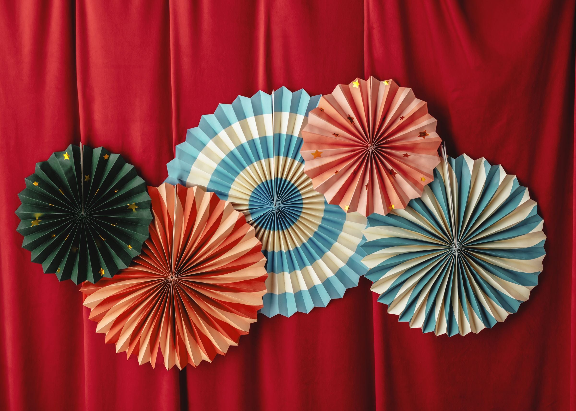 Vibrant carnival-themed paper fans displayed against a red stage curtain for a party backdrop.