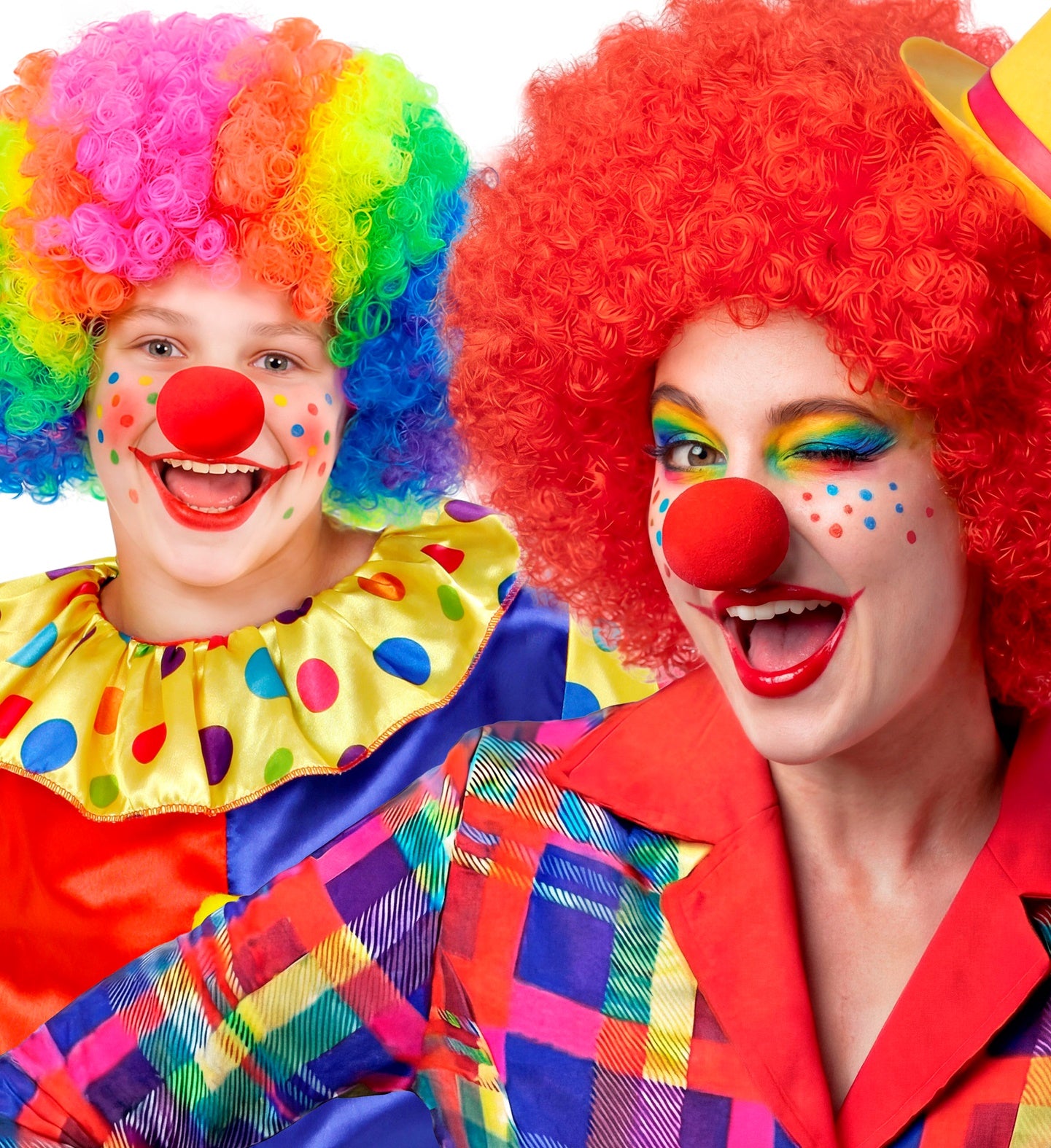 Two happy clowns posing together in bright, colorful circus costumes, featuring one in a rainbow curly wig and one in a red curly wig, both wearing classic red sponge clown noses.