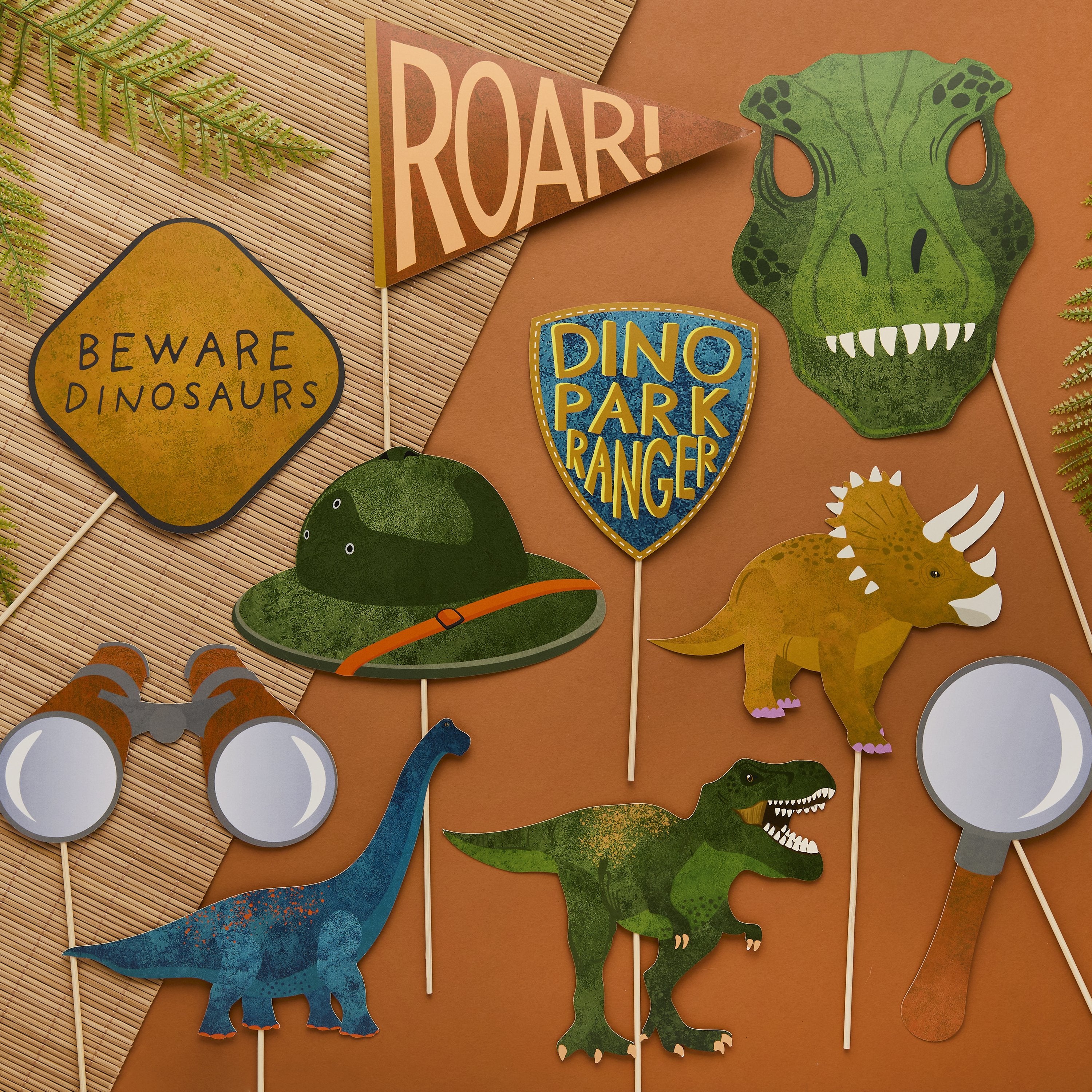 A set of 10 dinosaur party photo props including a T-Rex mask, explorer hat, binoculars, and a "Beware Dinosaurs" sign on an orange background.