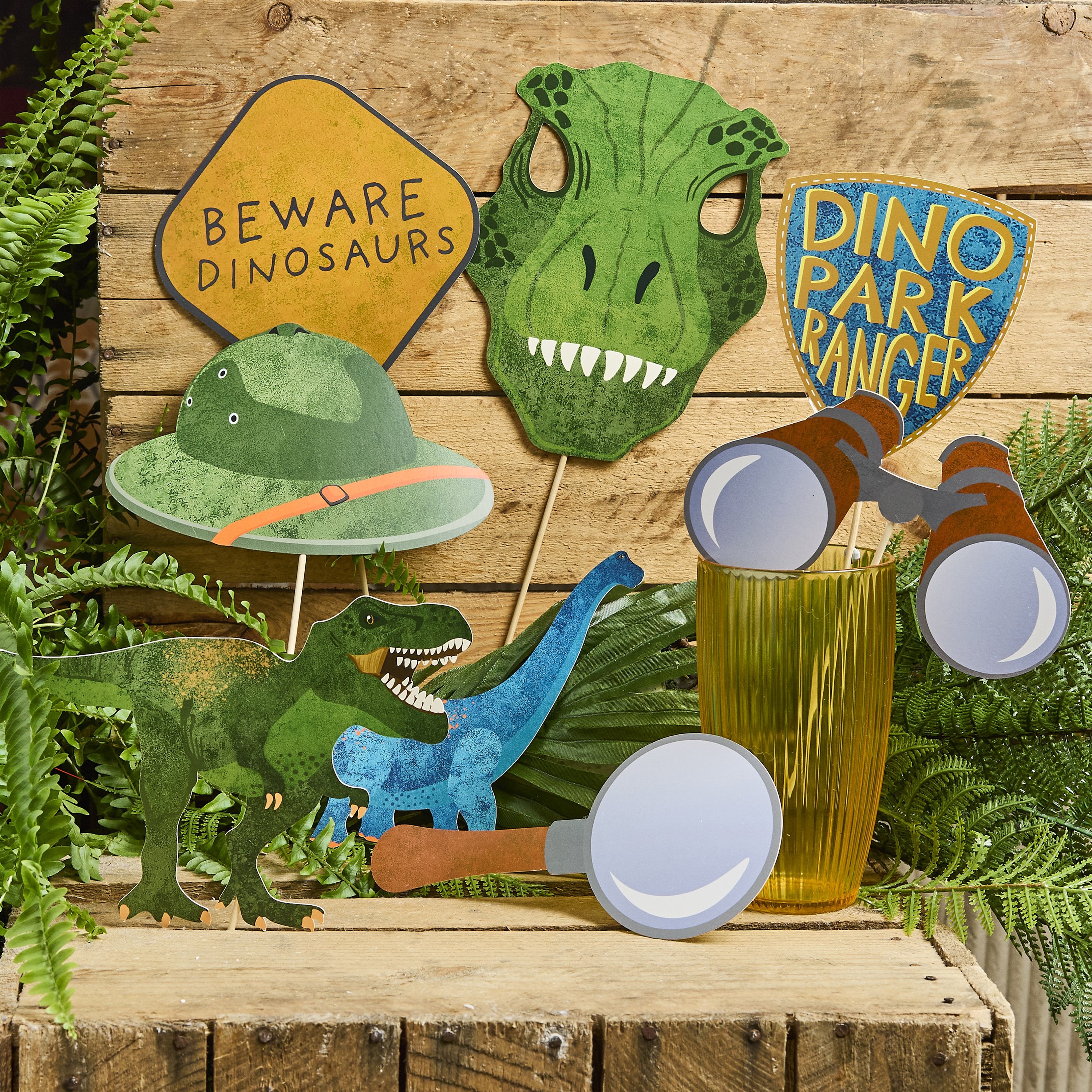 Dinosaur photo props displayed in a yellow glass among fern leaves and wooden crates, creating a legendary jungle atmosphere.