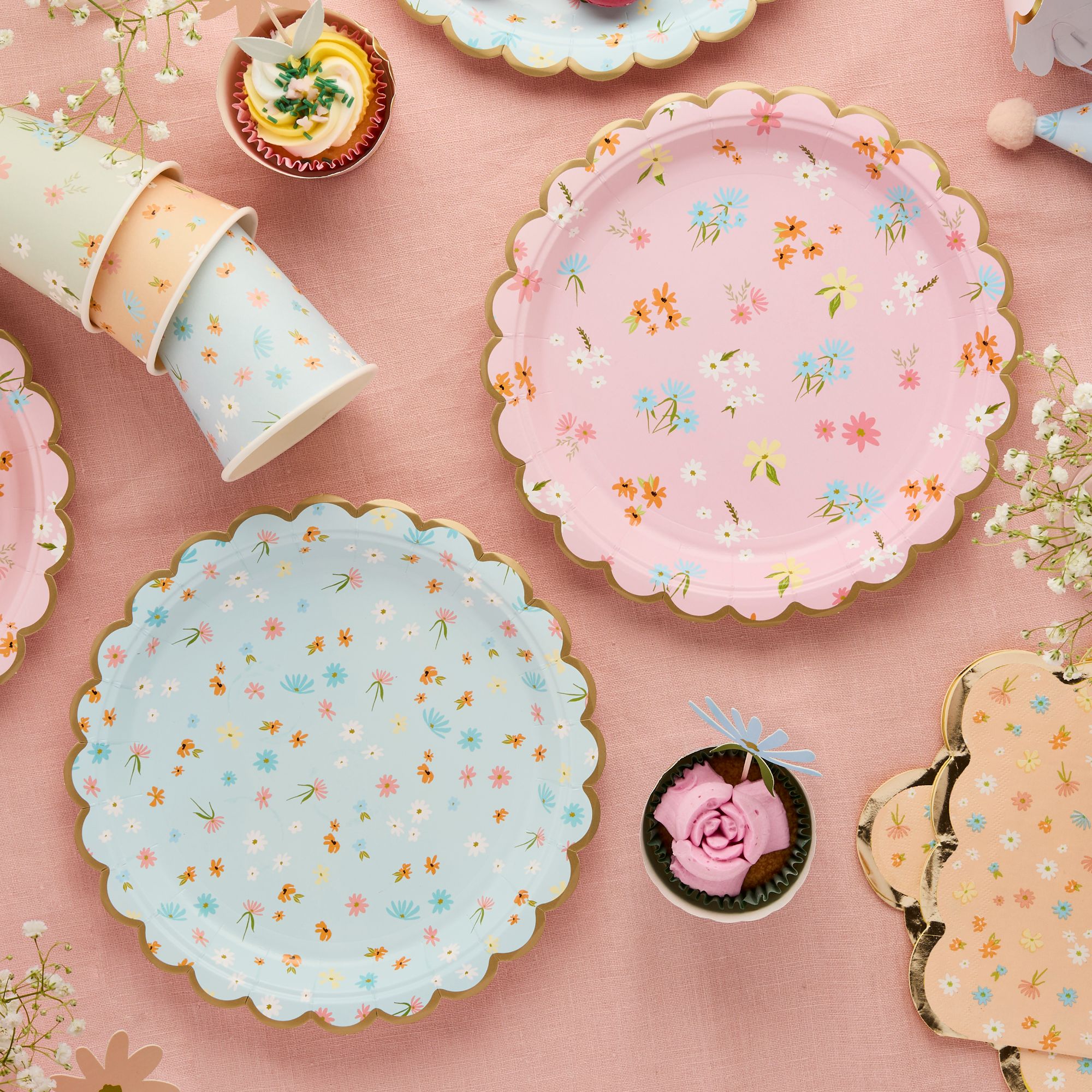 A close-up of pink and blue scalloped plates featuring dainty wildflower patterns at an outdoor brunch.