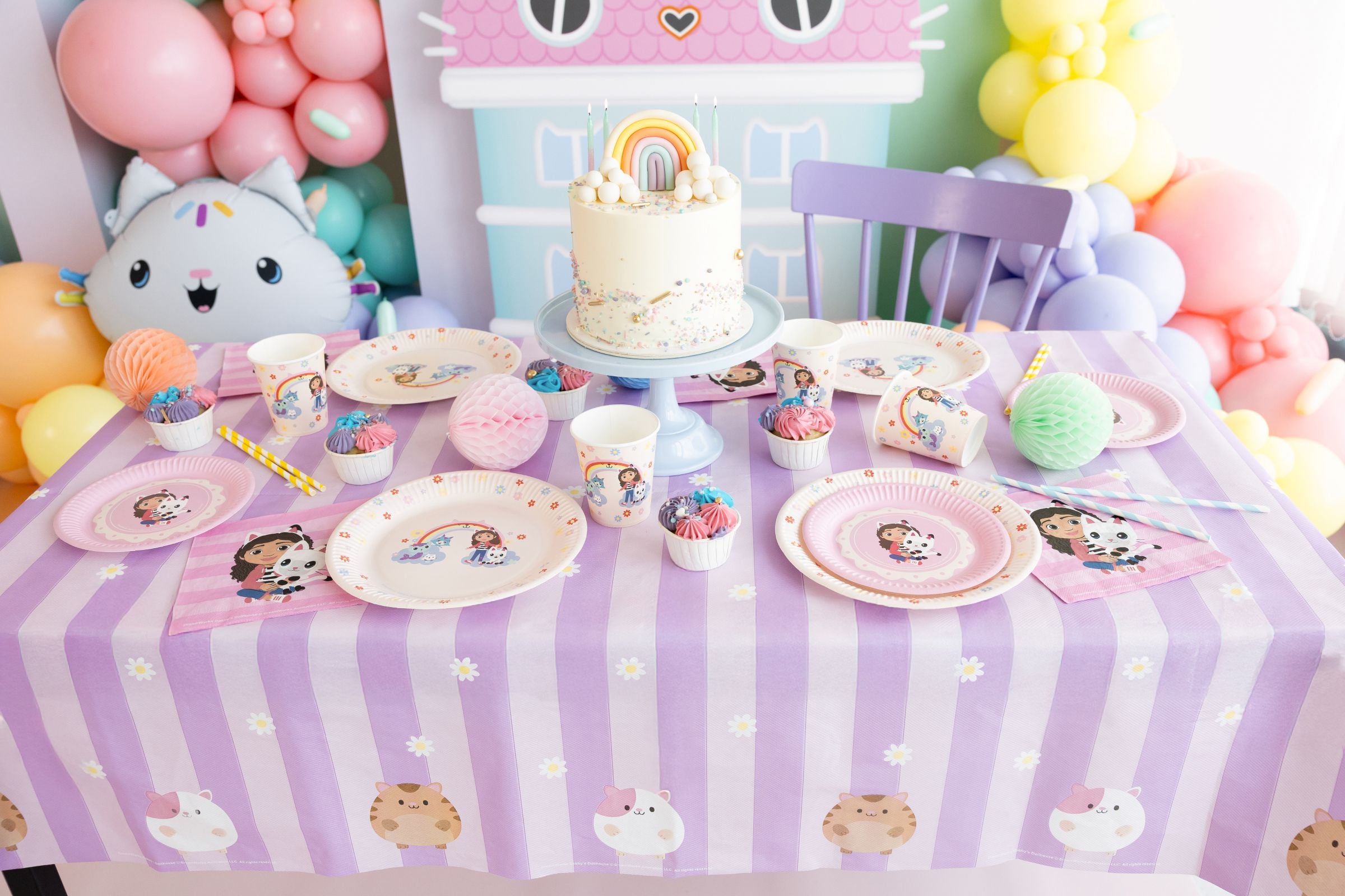 Gabby's Dollhouse themed birthday table setup with character tablecloth, plates, cups, and a rainbow cake.