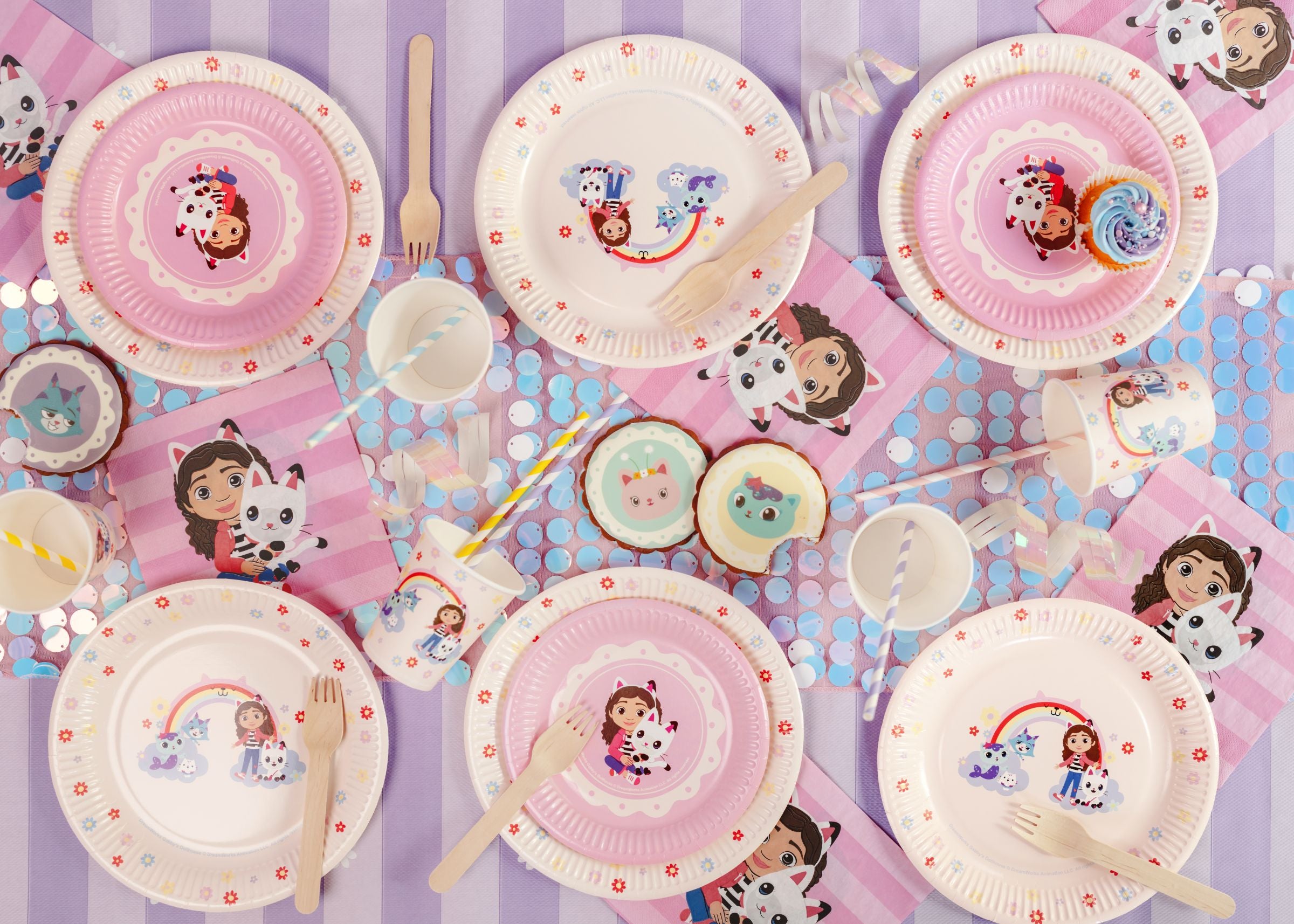 Children's Gabby's Dollhouse themed party tableware with cartoon character plates, cups, and cutlery on a polka dot background.