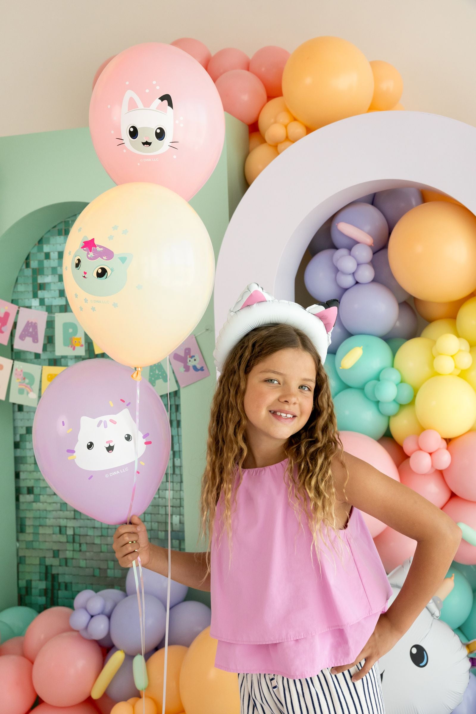 Young girl holding a bunch of Gabby's Dollhouse character balloons at a colorful birthday party.