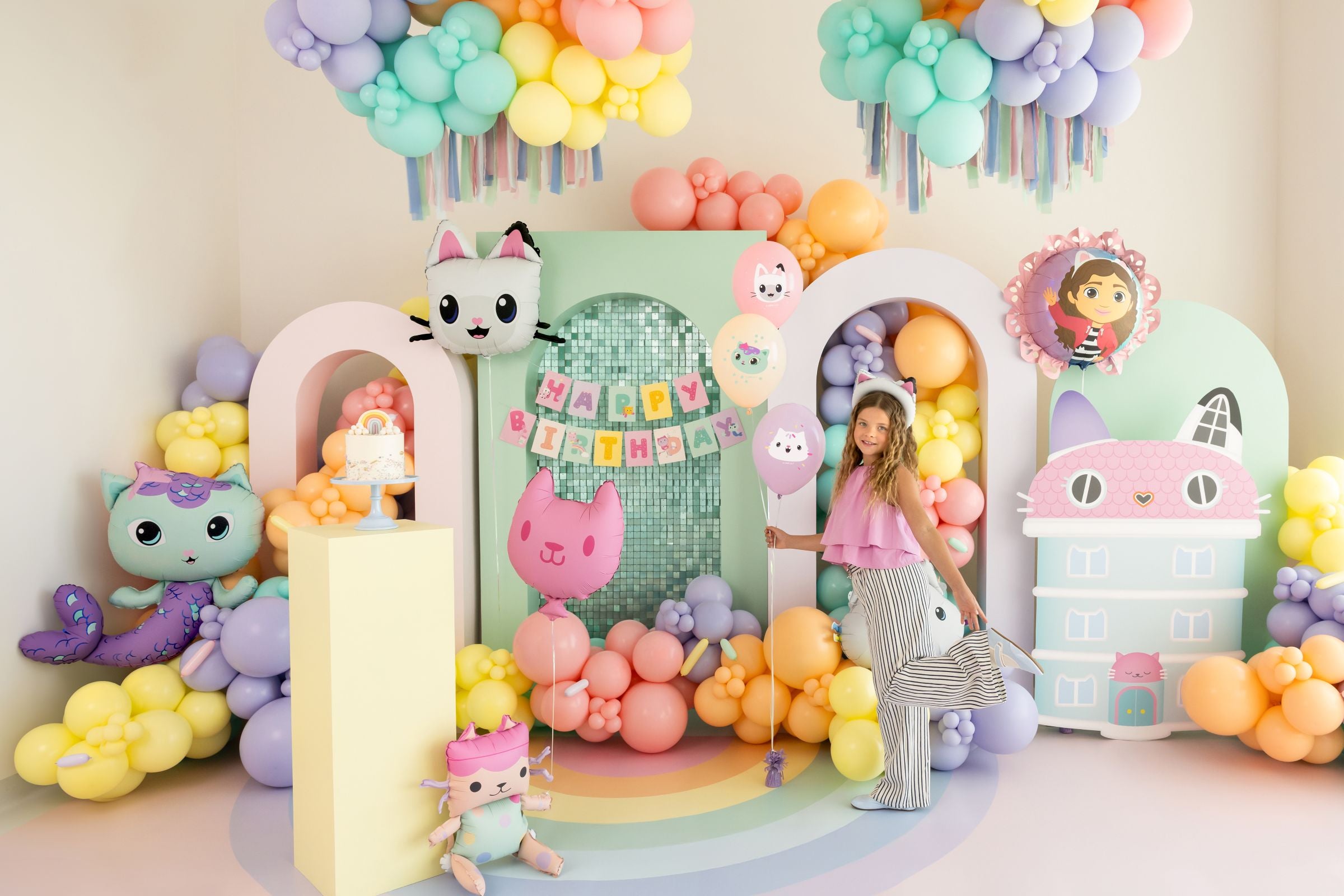 Large Gabby's Dollhouse themed birthday backdrop with pastel balloons, character cutouts, and cake.