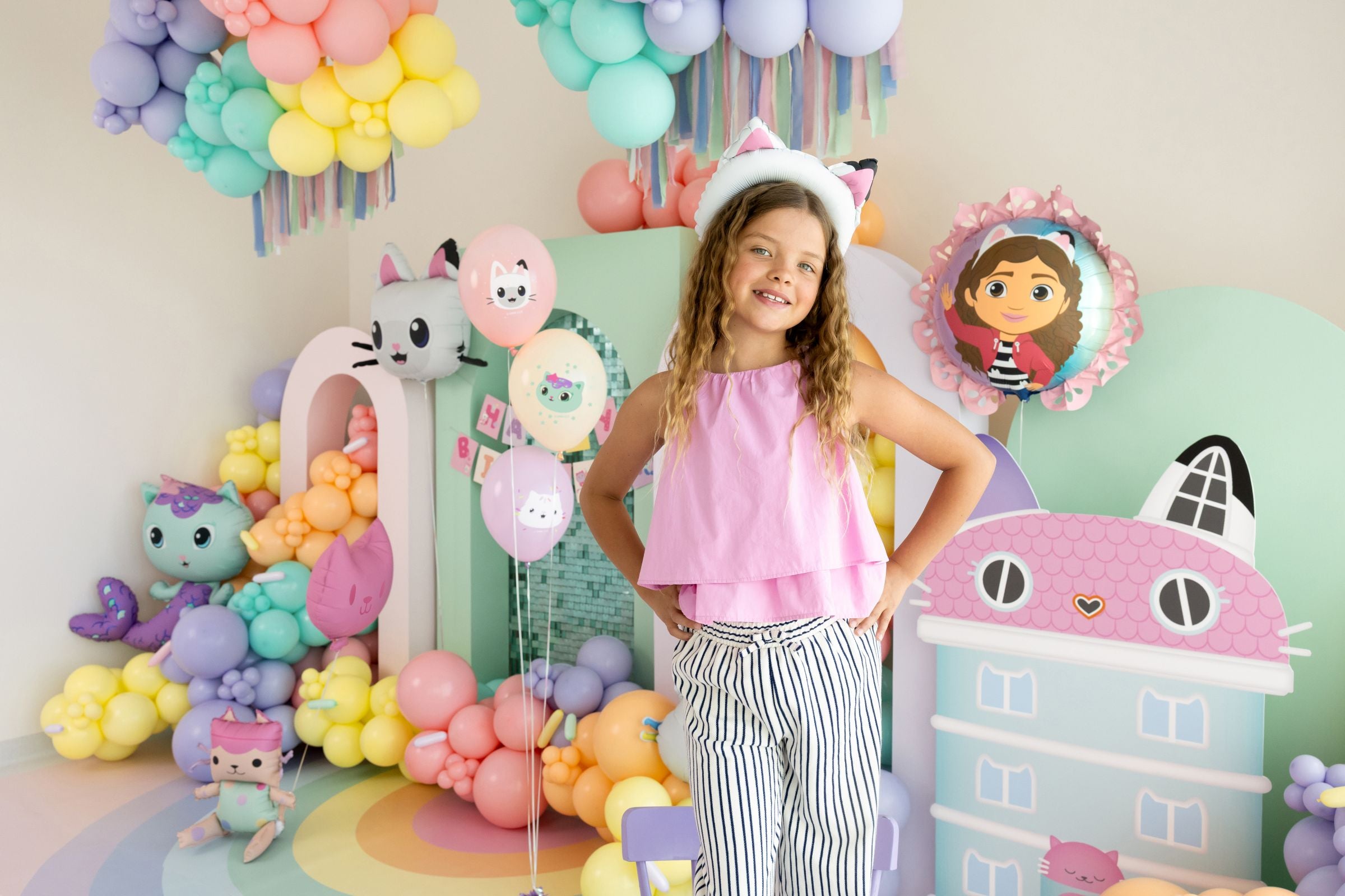 Child in a decorated room with colorful Gabby's Dollhouse balloons and cartoon character decorations