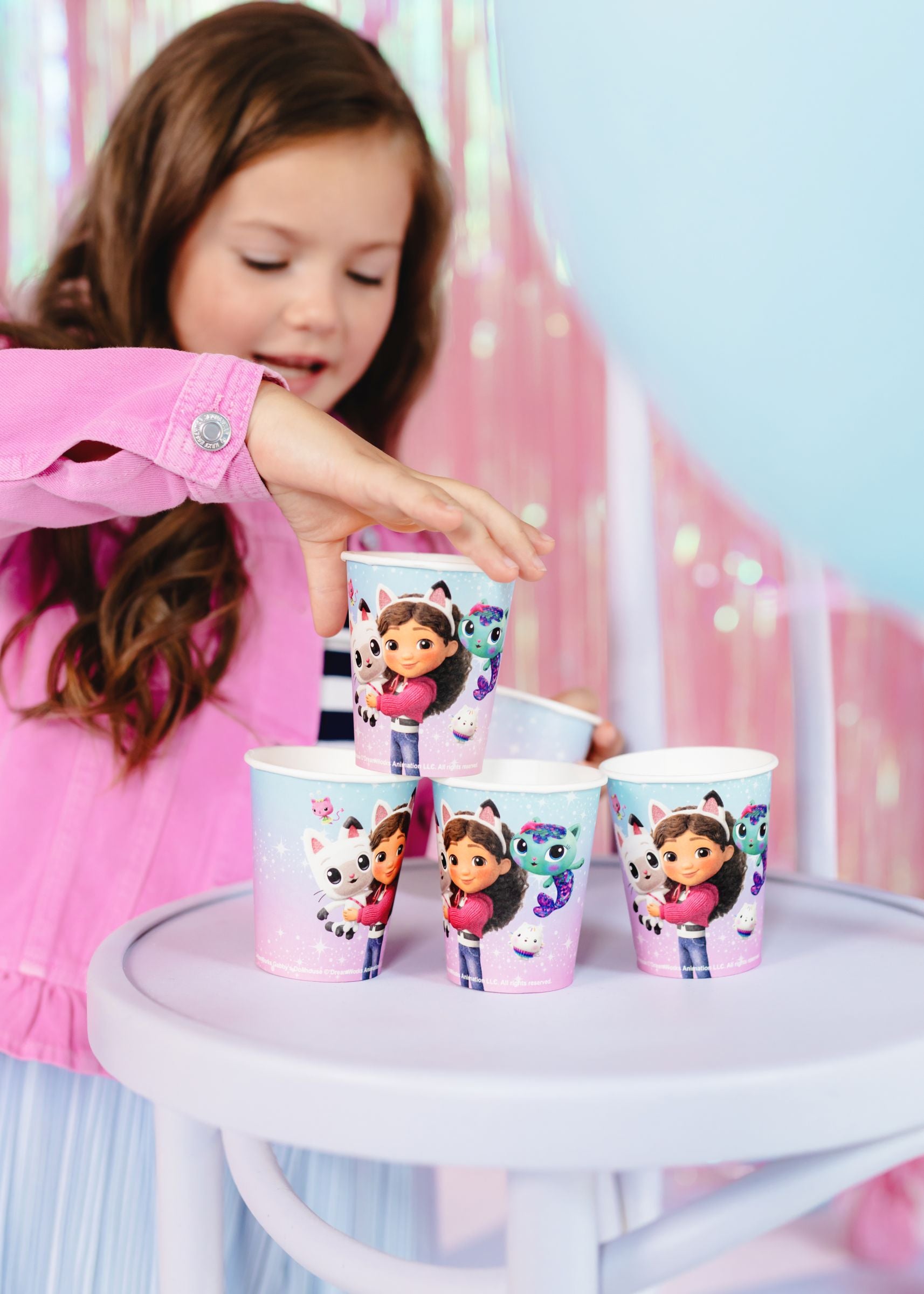 A young girl stacking Gabby's Dollhouse paper cups during a themed birthday celebration.