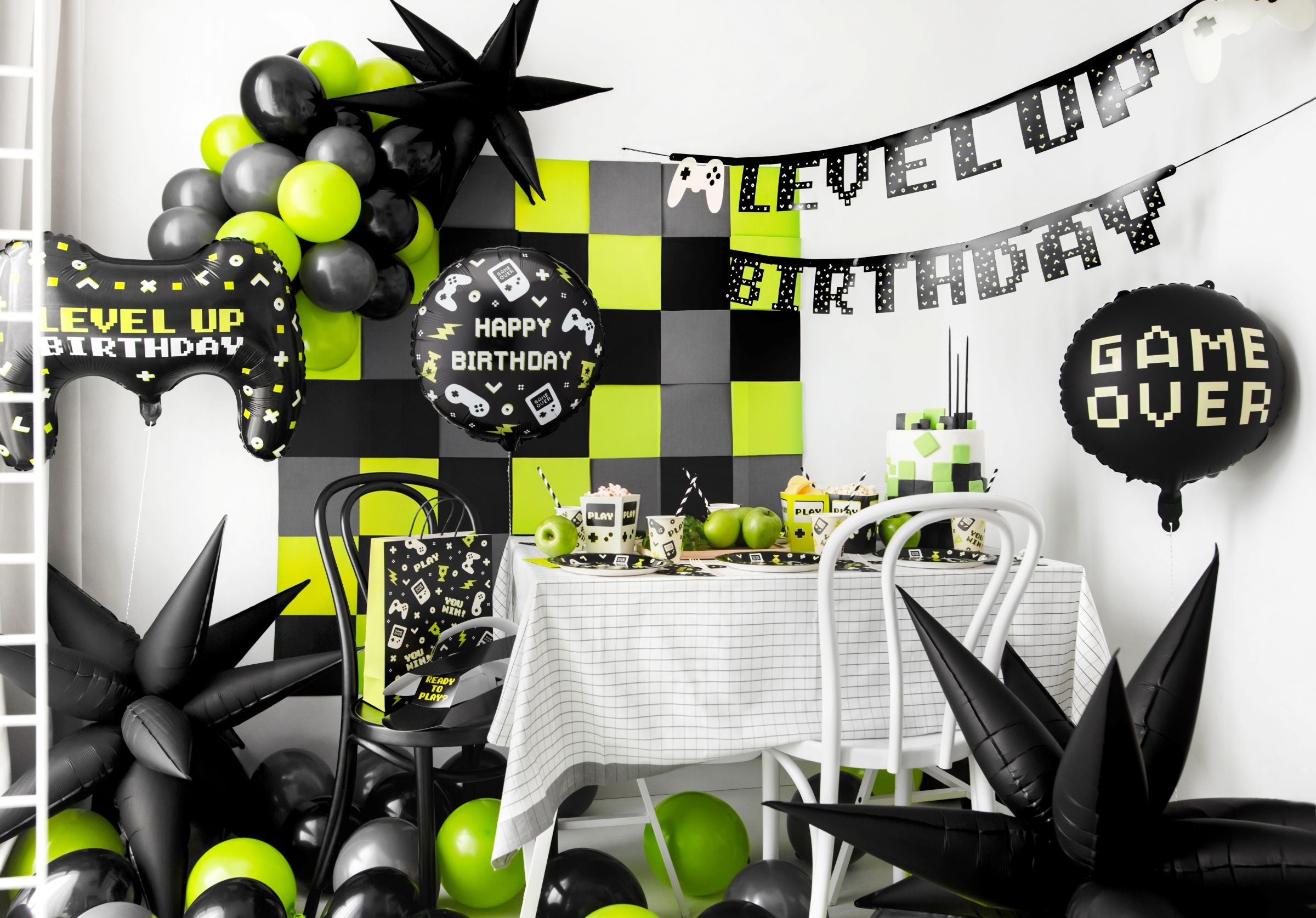 A gaming-themed party table featuring a black Happy Birthday gamer balloon alongside a Level Up banner and green balloons.