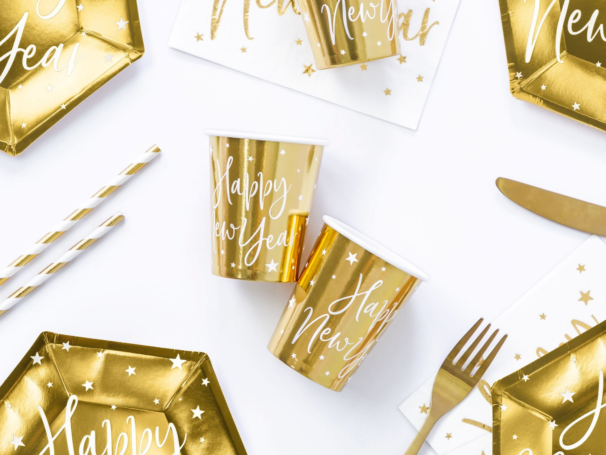 New Year's Eve party table with gold paper cups, gold hexagonal plates, and white napkins.