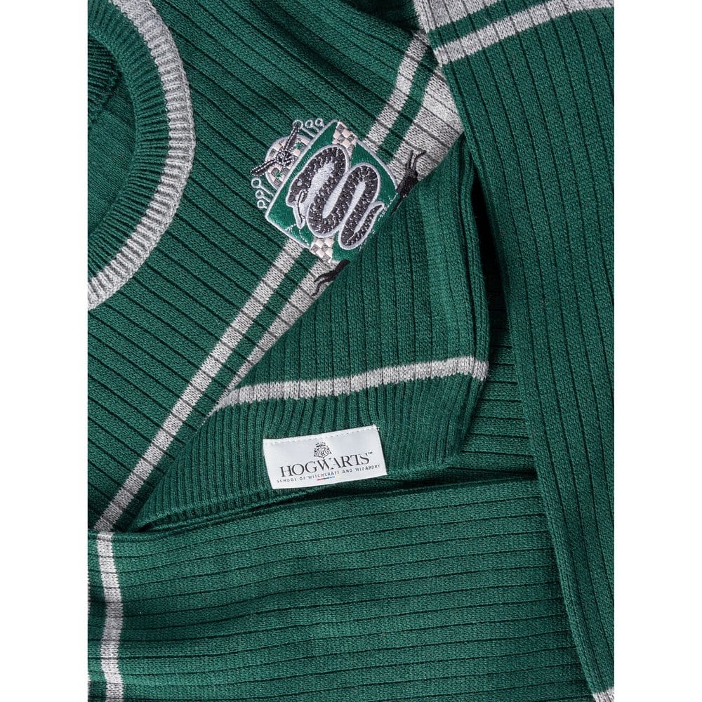 A close-up photograph of a green and grey striped Harry Potter Slytherin jumper, highlighting the high-quality embroidered serpent house crest and the official Hogwarts School of Witchcraft and Wizardry hem tag.