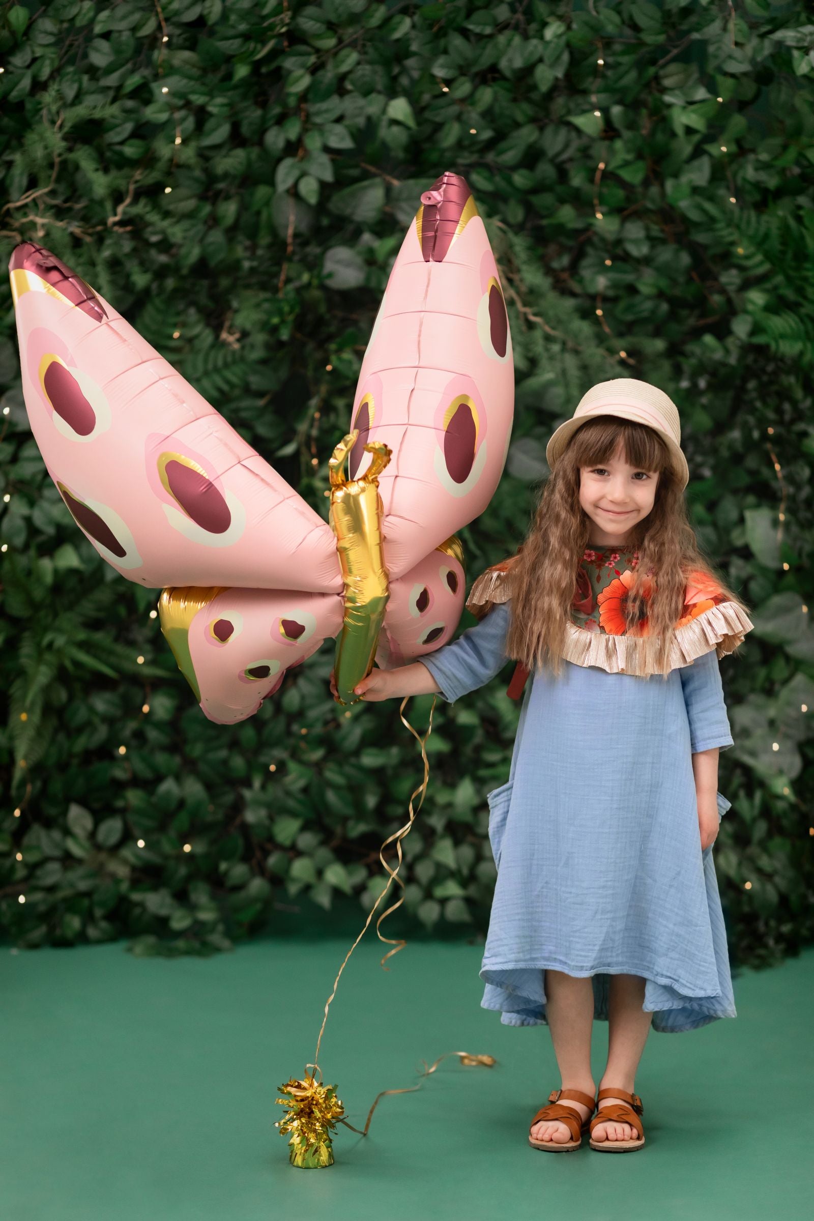 Child holding a large butterfly-shaped balloon against a green background