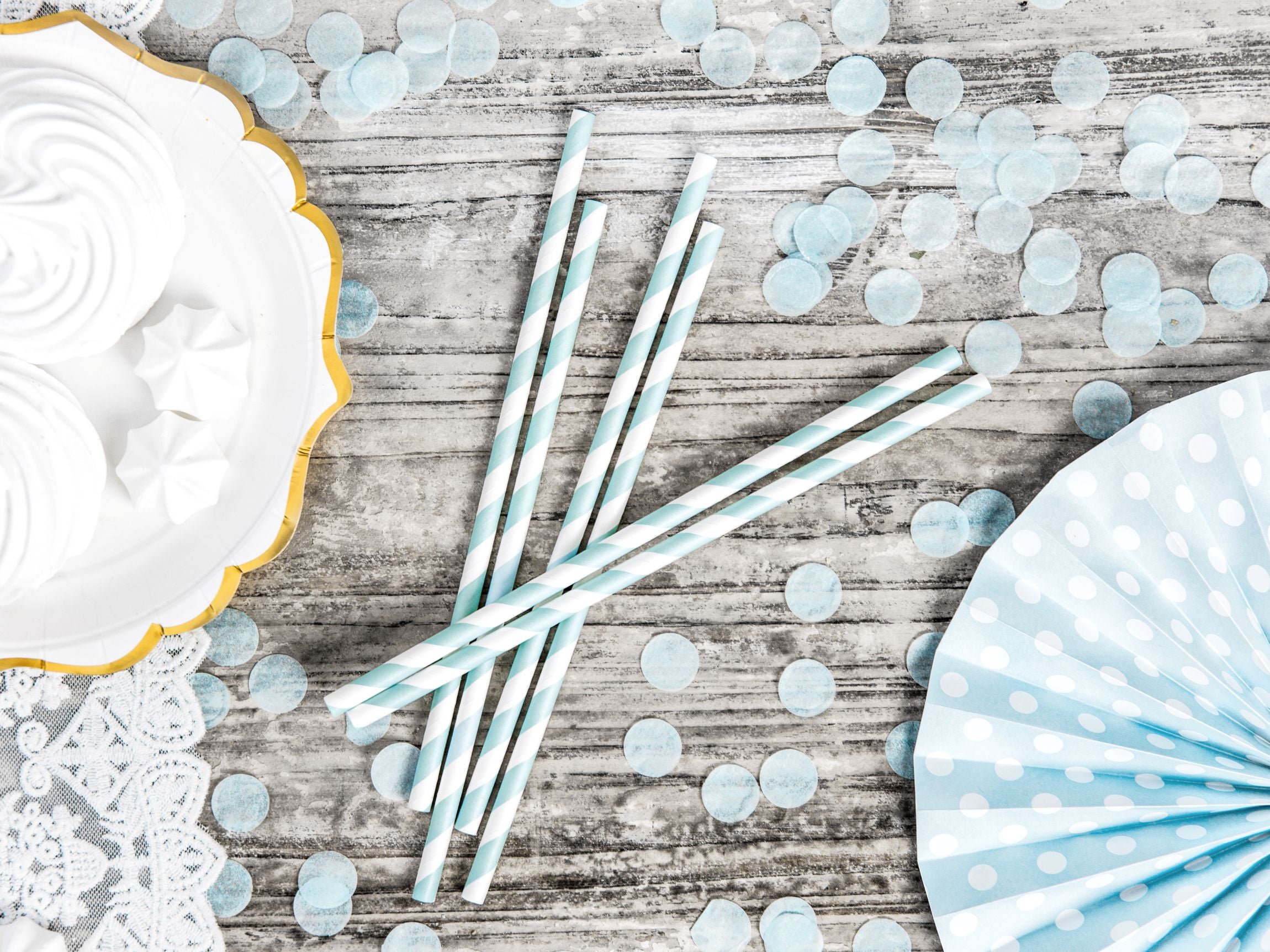 Light blue striped paper straws placed next to white party treats and blue confetti.
