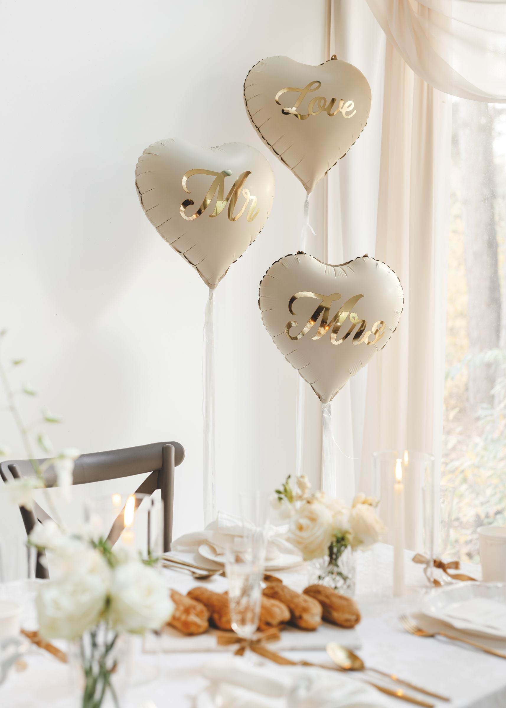 A romantic wedding breakfast setup featuring floating Mr, Mrs, and Love heart balloons in beige and gold.