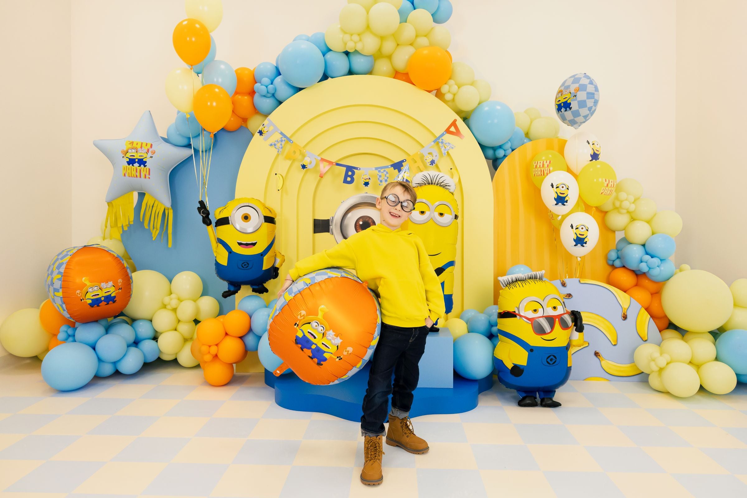 Minion Ron foil balloon shown with a child at a fully decorated Minions-themed birthday party.