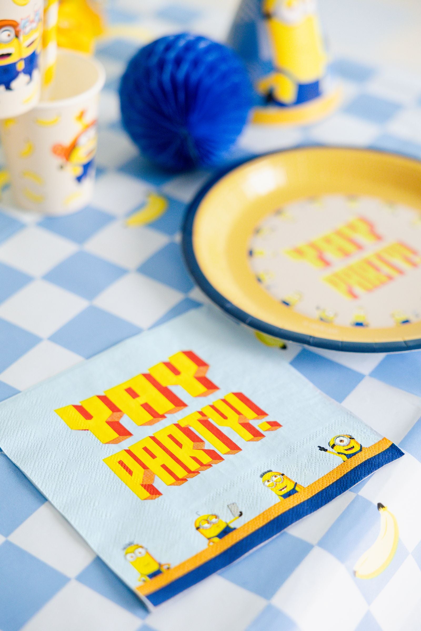 A checkered blue and white tablecloth decorated with Minions napkins, plates, and blue honeycomb decorations.