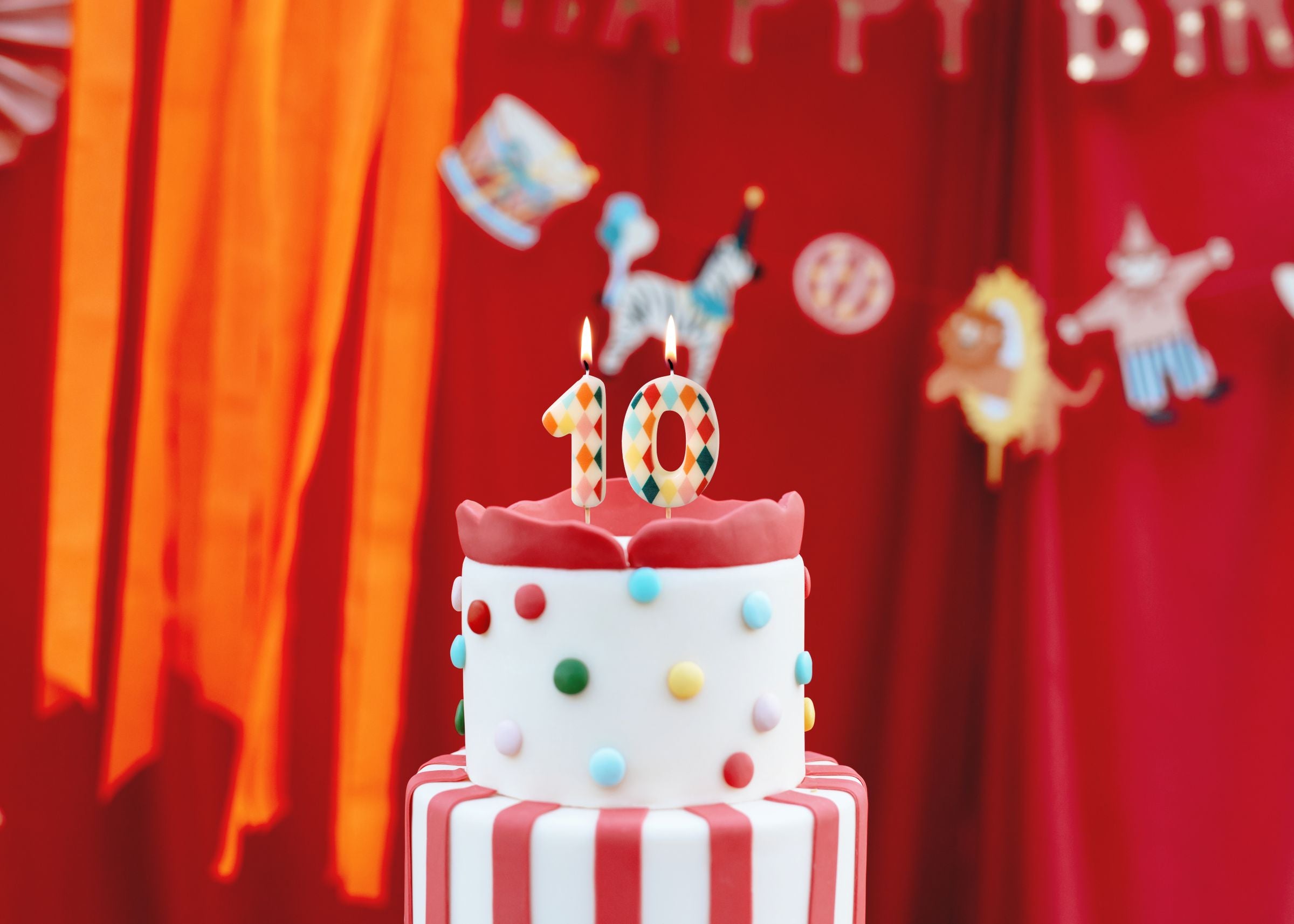 A lit number 10 made of rhombus patterned candles sitting on top of a red and white striped circus-themed cake.