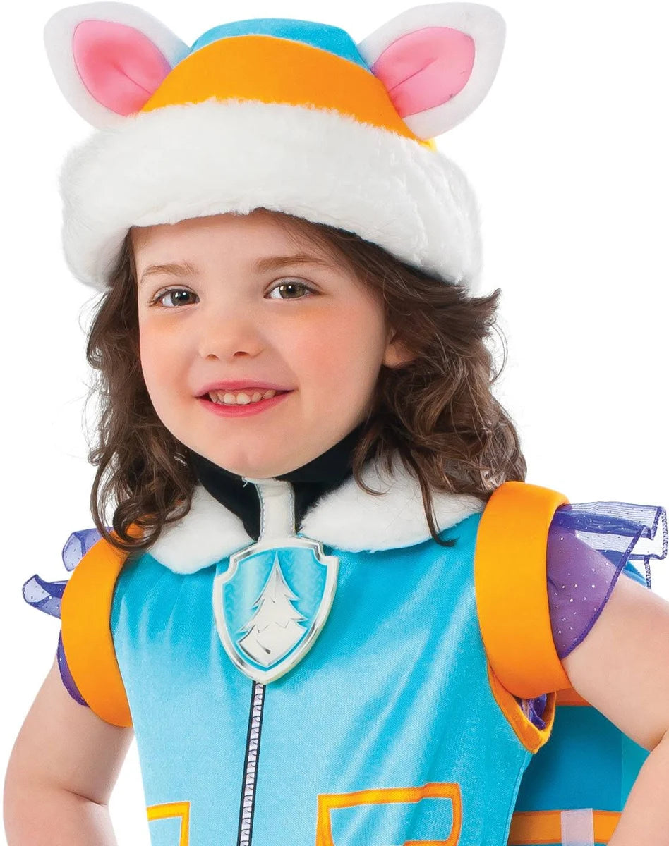 A close-up portrait of a smiling child wearing an officially licensed Paw Patrol Everest fancy dress costume, highlighting the blue winter vest design, the silver pine tree pup tag, and the teal hat with fluffy white trim and pink husky ears.