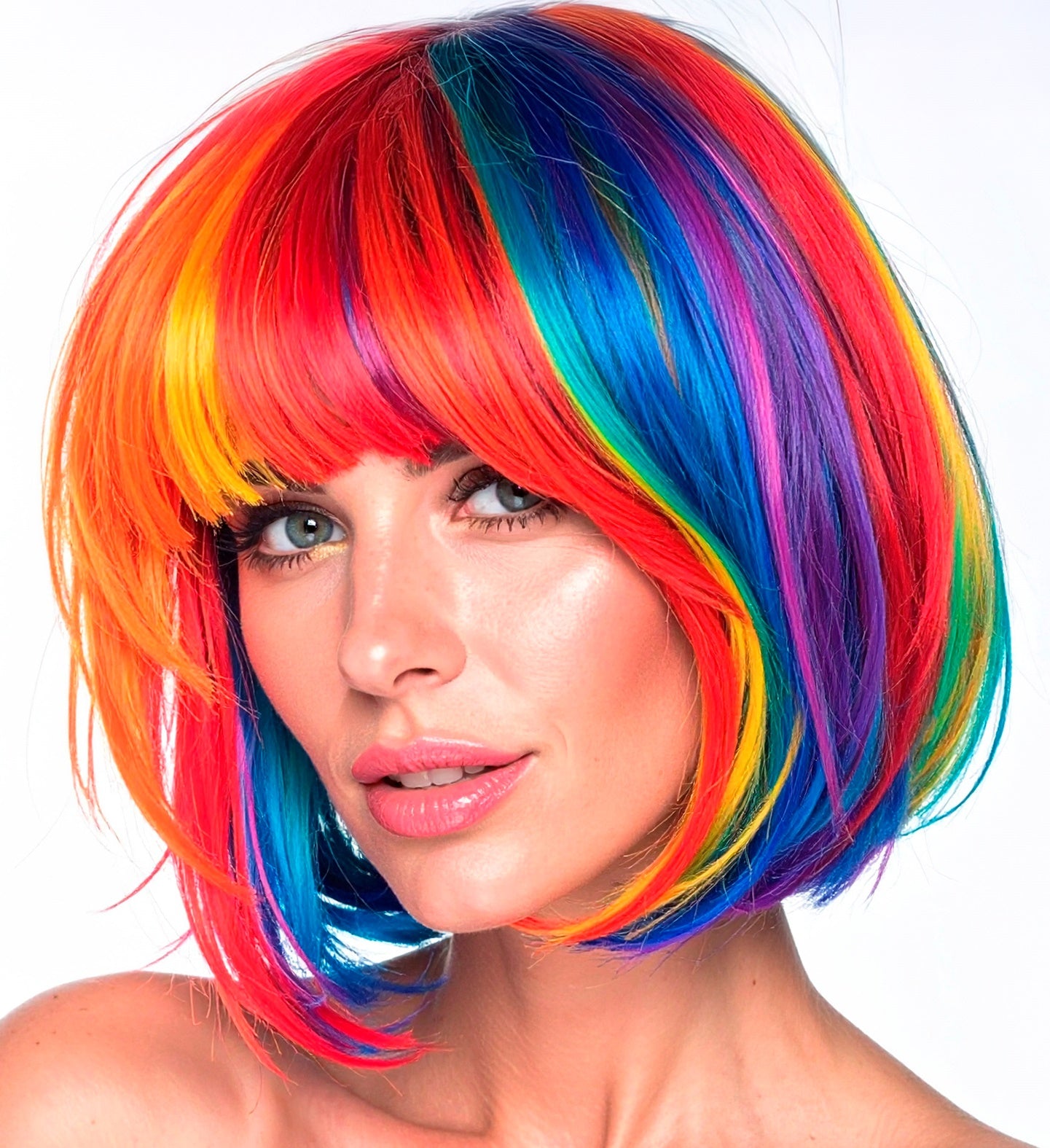 A woman with green eyes and pink lipstick models a vibrant, short rainbow bob wig with a full fringe.