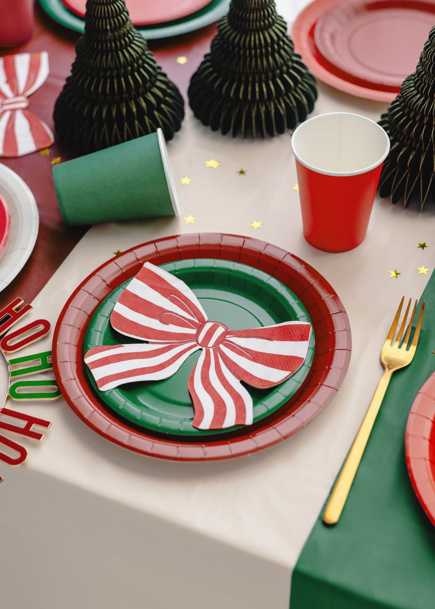 A festive Christmas table setting using red and dark green paper plates and cups, with honeycomb decorations.