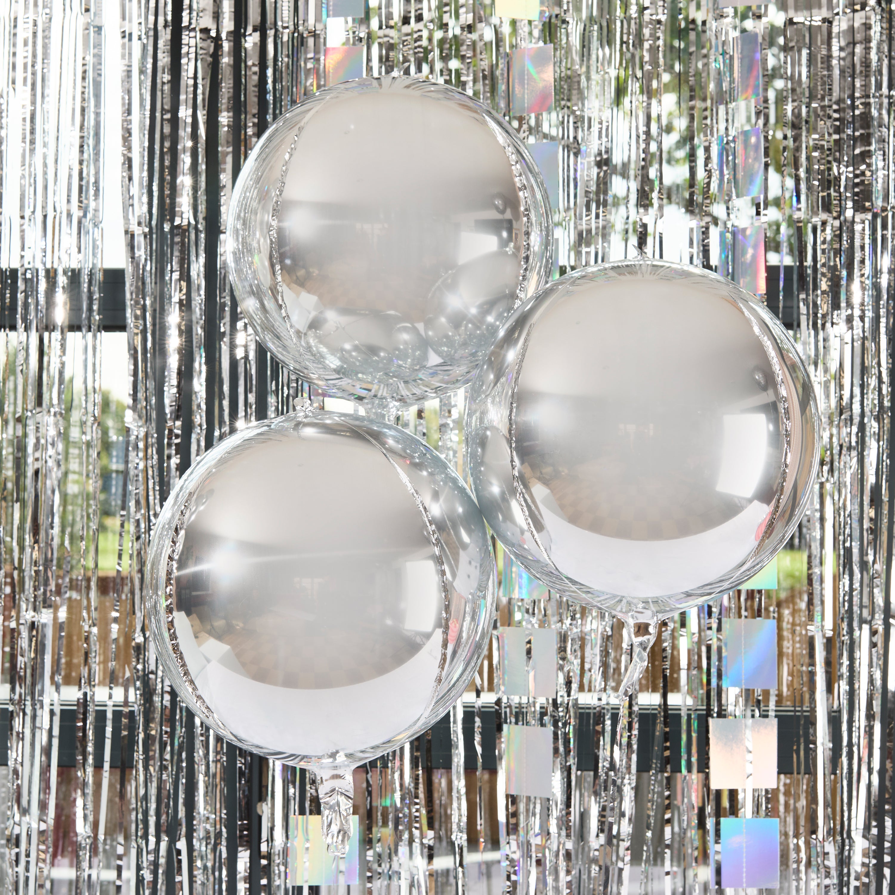 Three shimmering silver orb balloons floating against a tinsel backdrop at a disco party.