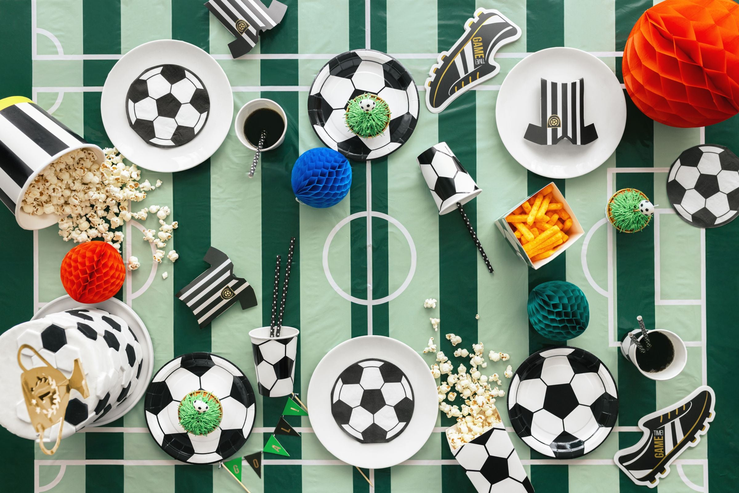 Table setting with soccer-themed decor including plates, cups, and decorative items on a green and white striped tablecloth.