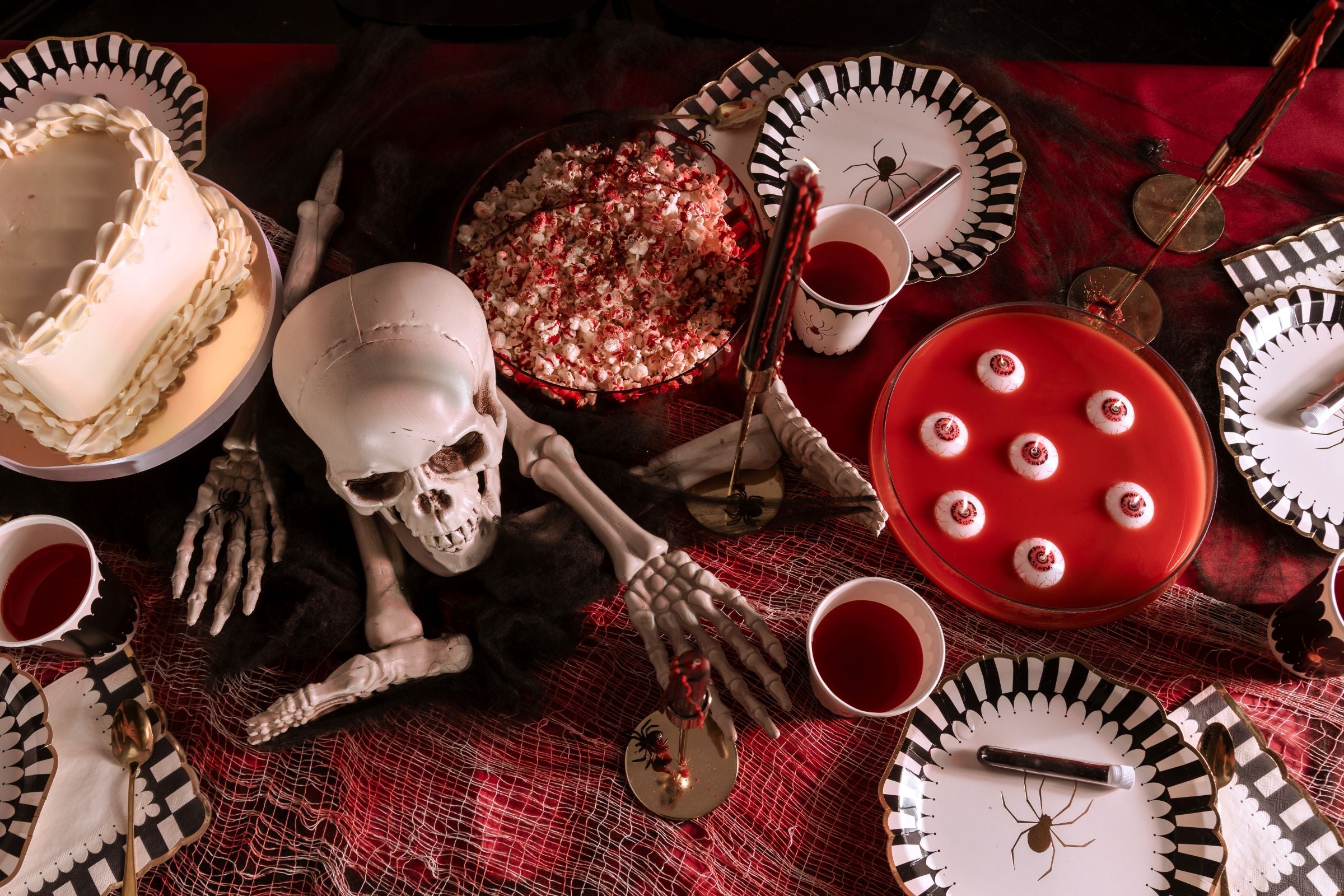 Halloween-themed table setting with skeleton, skull, and decorative items on a red tablecloth.