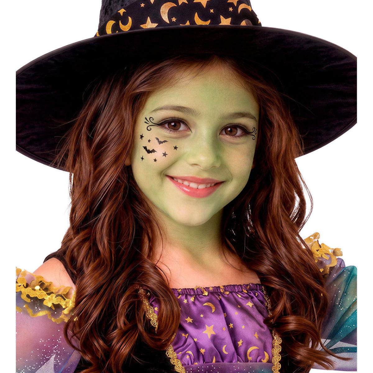 A smiling young girl wearing a witch hat and costume, featuring a light green makeup base and small black bat and star details painted on her cheek.