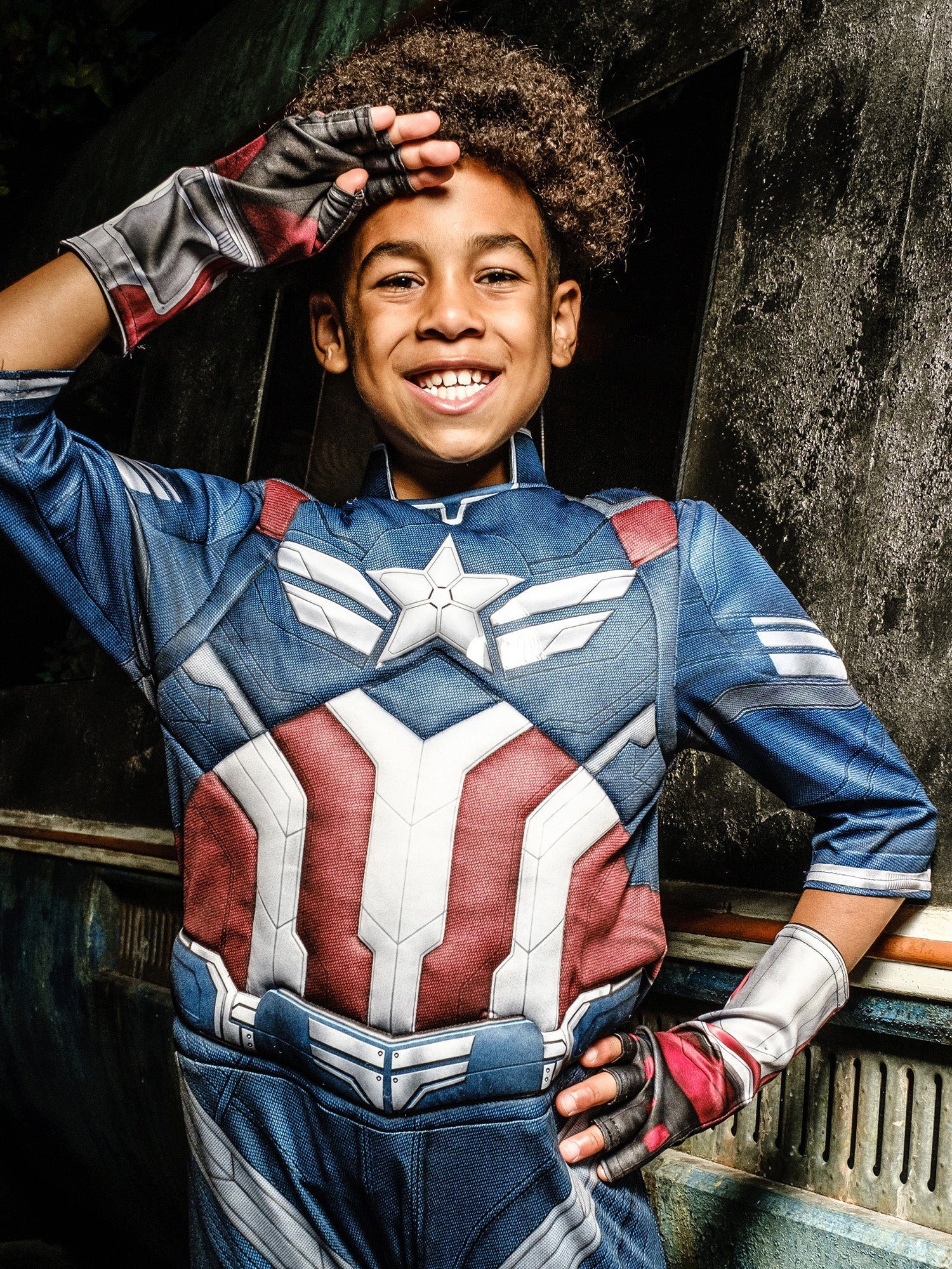 Child wearing a superhero costume with a star emblem, standing against a dark background.