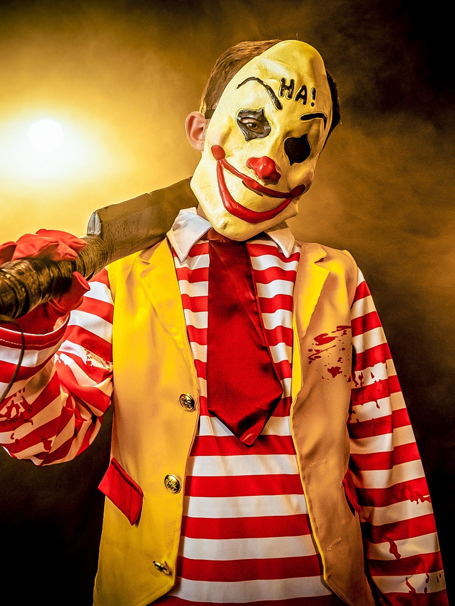 Person in a clown costume holding a knife with a dark, smoky background