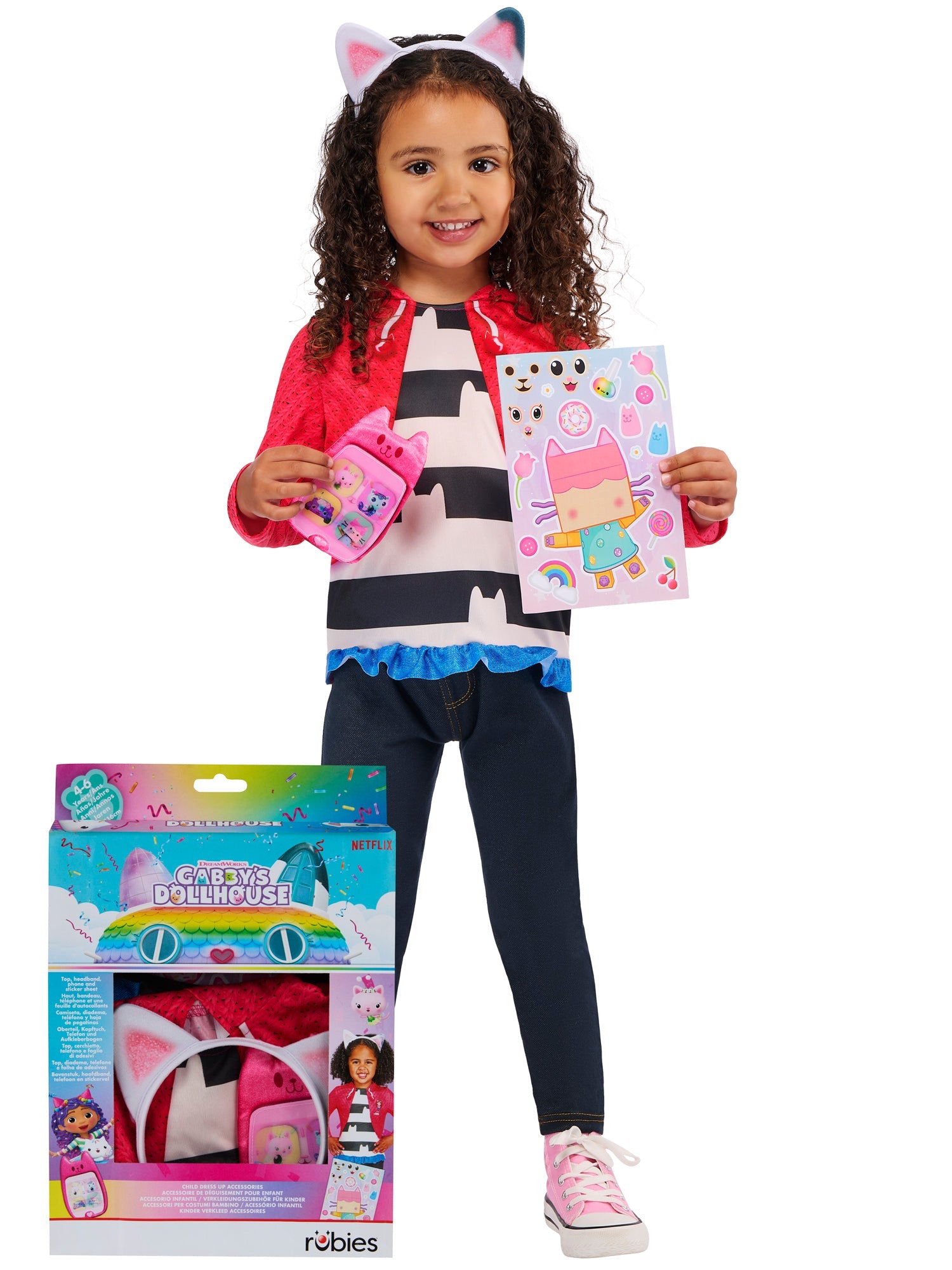 A smiling child wearing a Gabby's Dollhouse costume top, jacket, and cat-ear headband, holding a sticker sheet and plush toy phone, standing next to the official Gabby's Dollhouse display box.