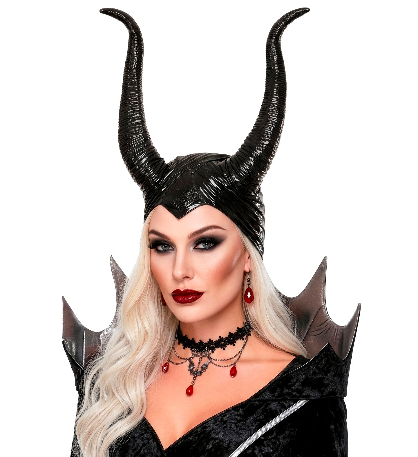 A model with long blonde hair wearing a black textured villain headpiece with tall horns, styled with a high-collared silver and black dress and bat-themed jewelry.