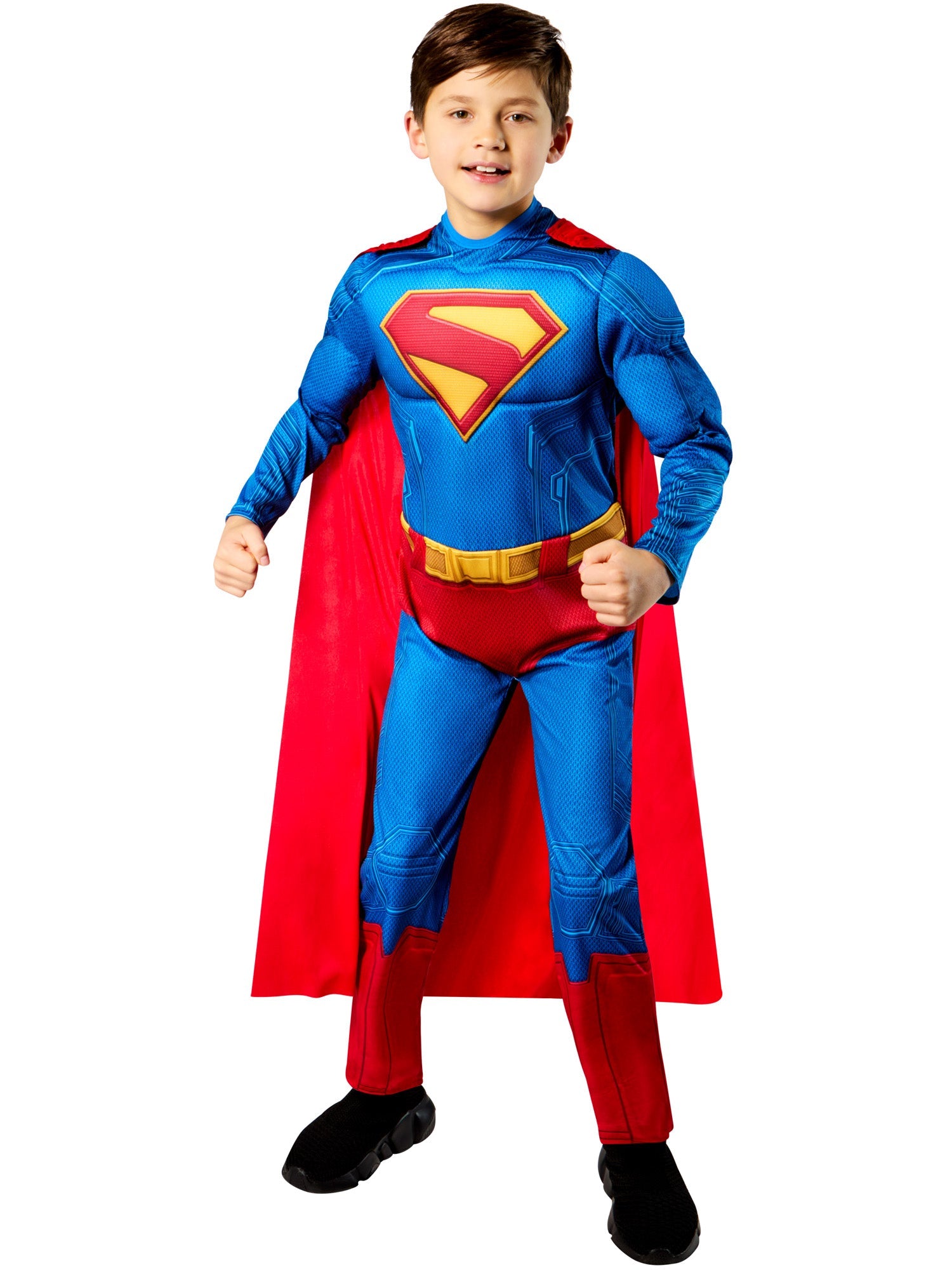A front-on view of a child in a Superman costume, smiling with one hand on their hip and the other in a fist, wearing the padded jumpsuit and a red cape.