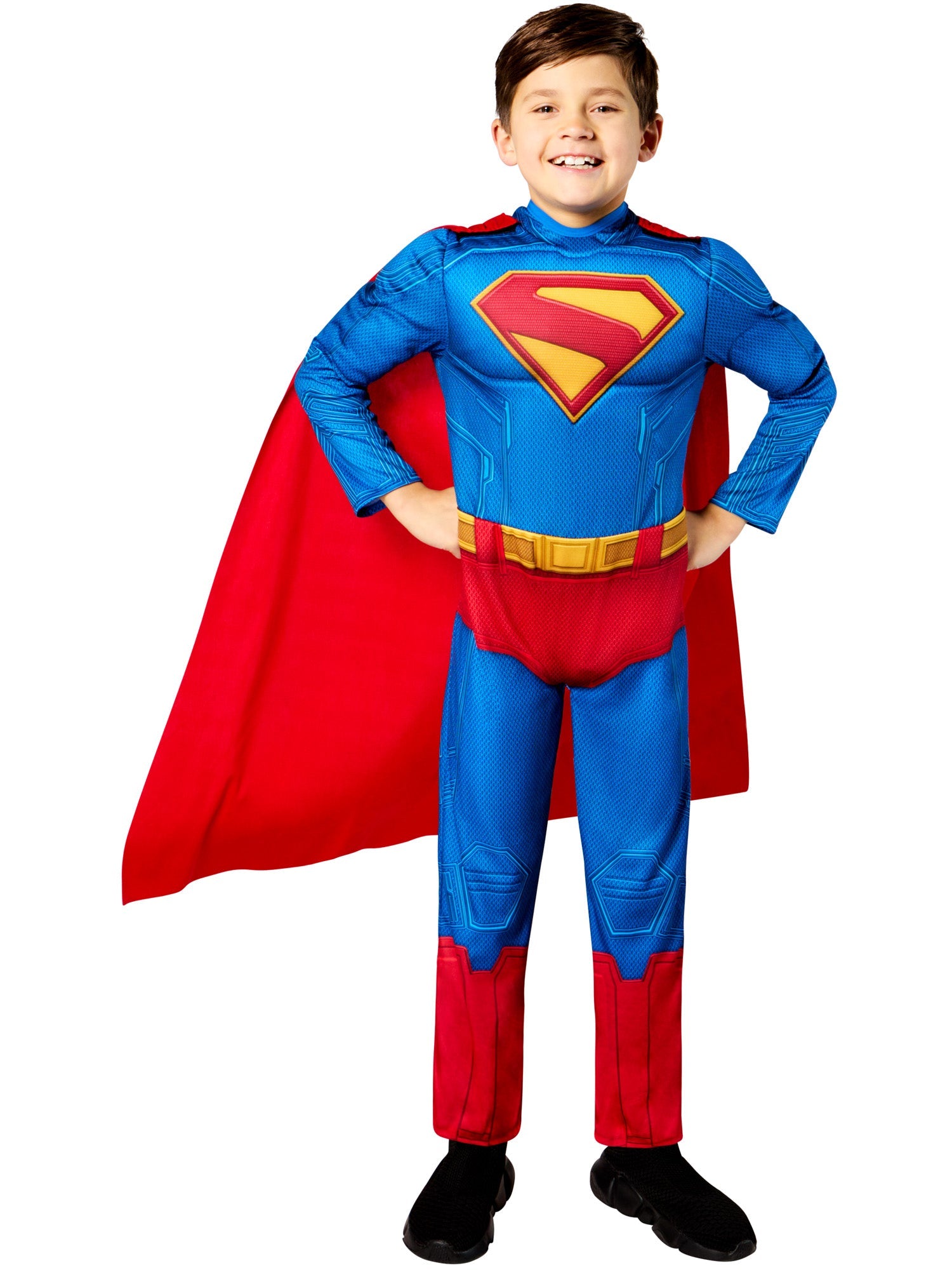 A child in a Superman costume, smiling with their hands on their hips, wearing the padded blue and red jumpsuit and a flowing red cape.