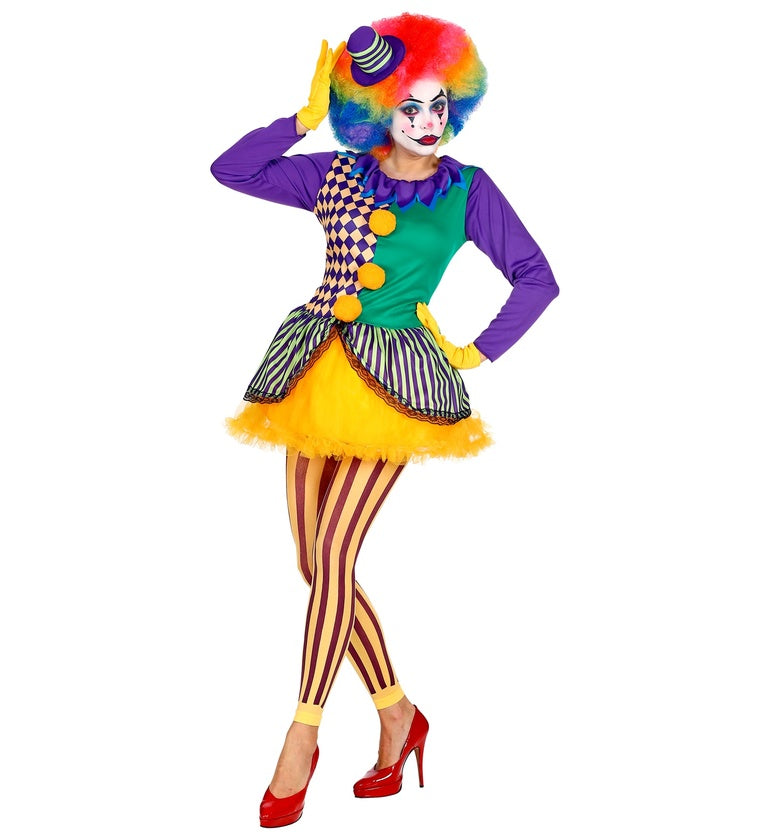 A lady in a colorful clown costume, posing with one hand on their hip and the other on their hat. The costume includes a purple, green, and checkered top, an orange tutu skirt, yellow and brown striped leggings, and a rainbow wig with a mini top hat.