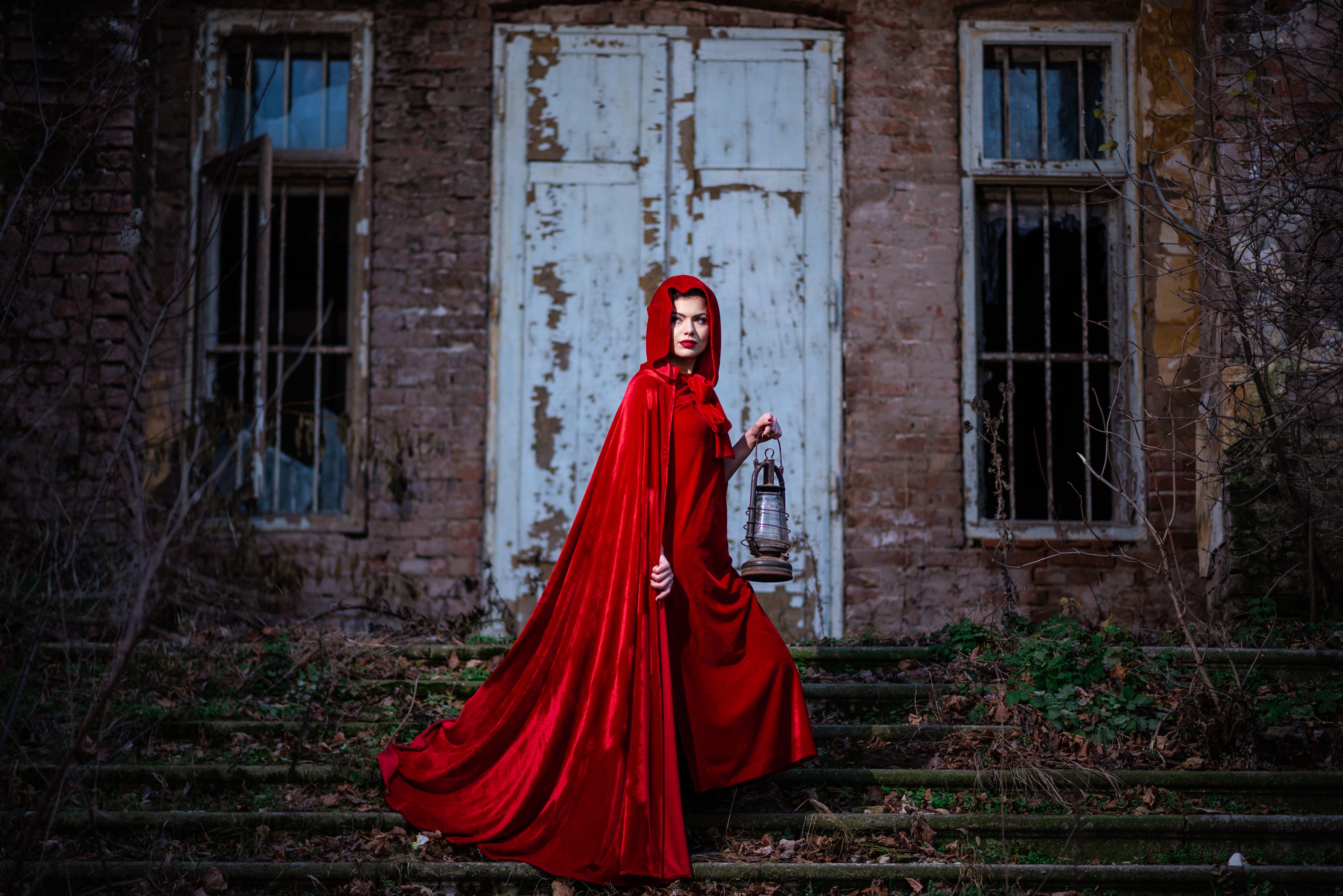 Woman in a long red cloak on steps of derelict building