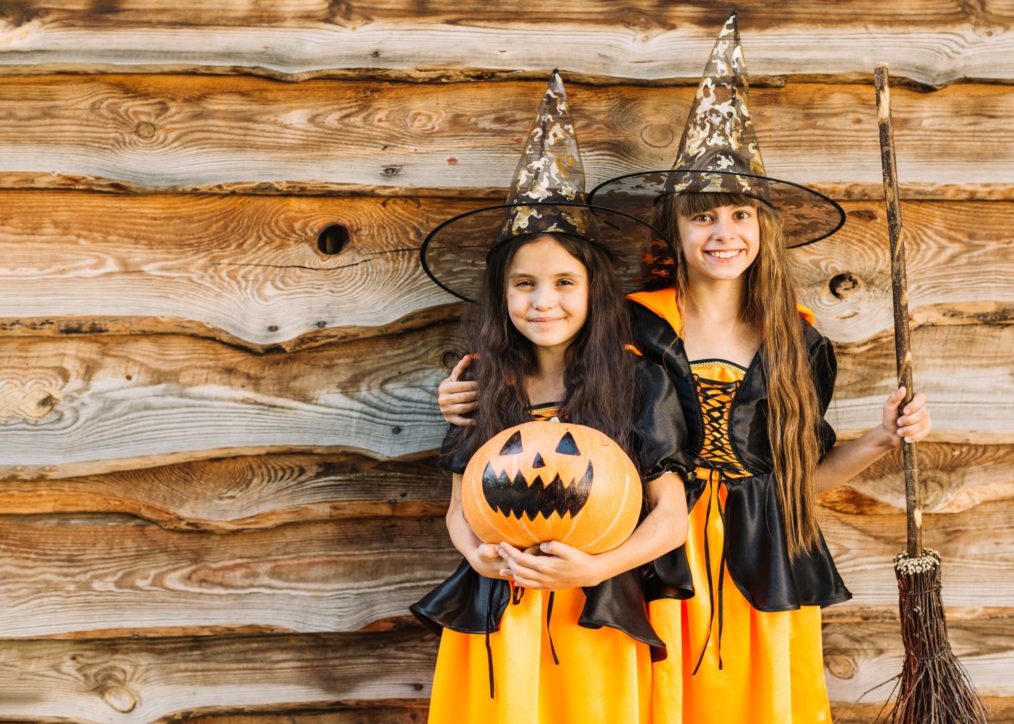 Two children dressed as witches, one holding pumpkin and the other holding a broom stick.