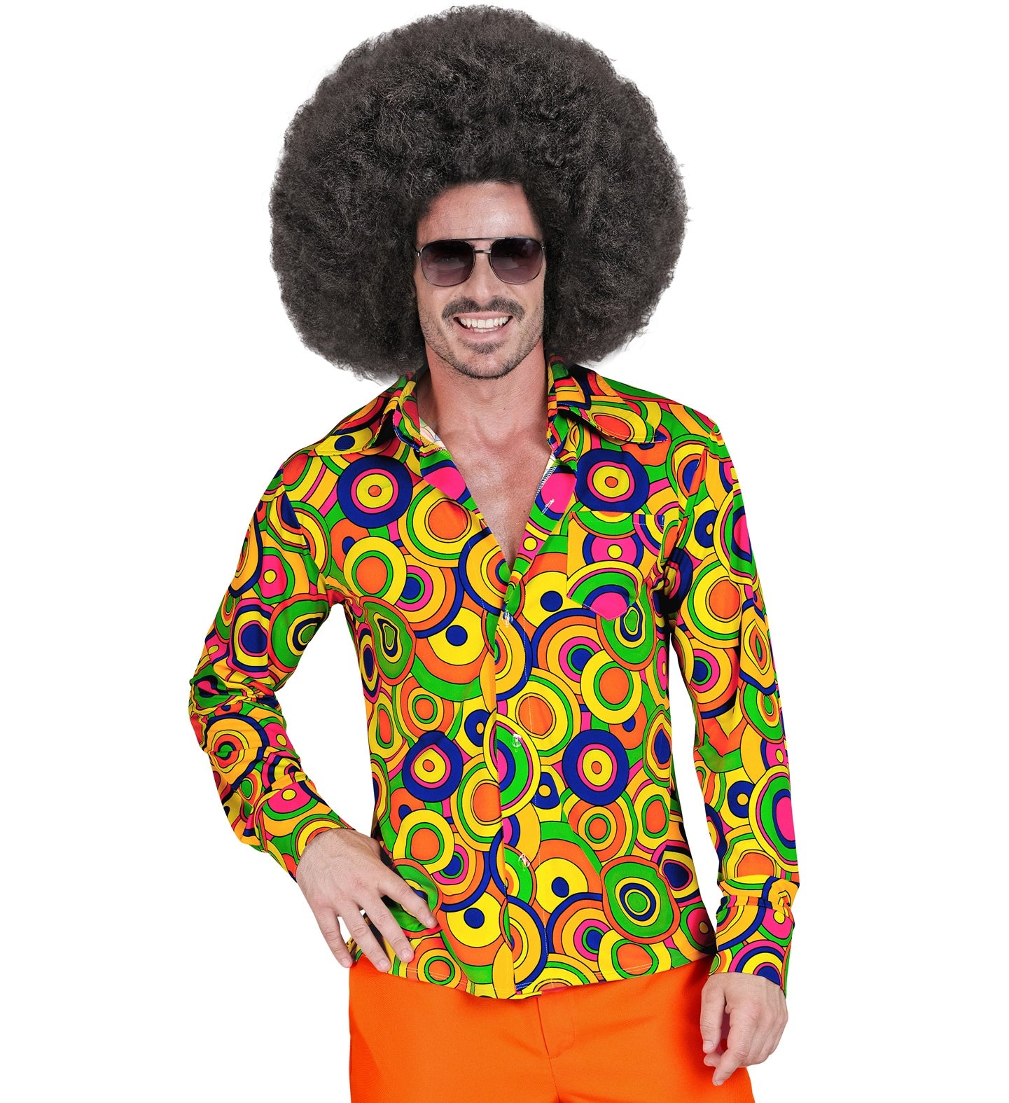 A smiling male model wearing a bright, psychedelic 1970s fancy dress button-down shirt featuring a colorful retro circle pattern and a wide collar, accessorized with bright orange trousers, aviator sunglasses, and a large afro wig.