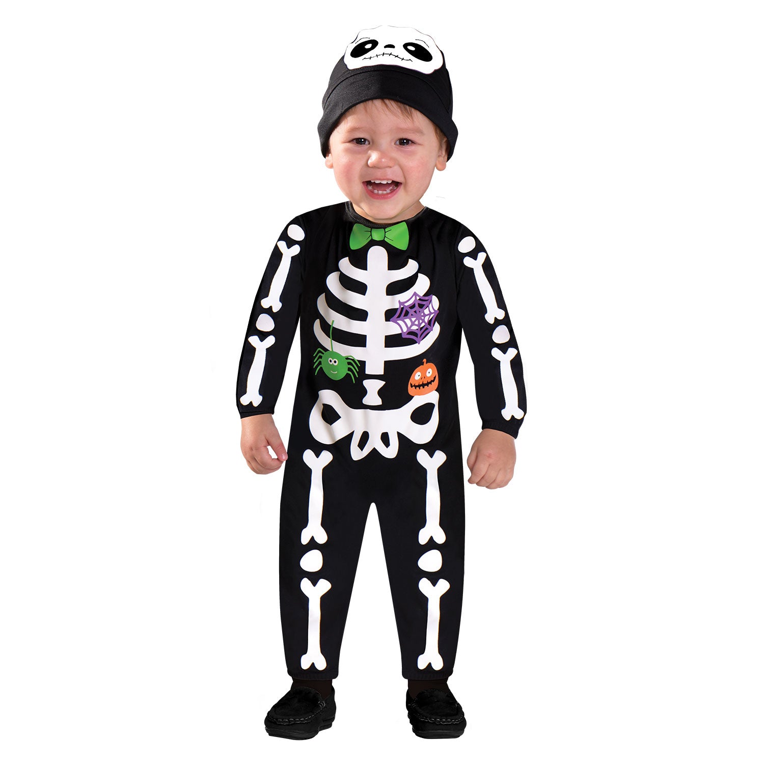 A smiling toddler child wearing a black jumpsuit with a printed white skeleton on the front, a green bowtie, and a matching black hat with a smiling skull design, standing against a white background.