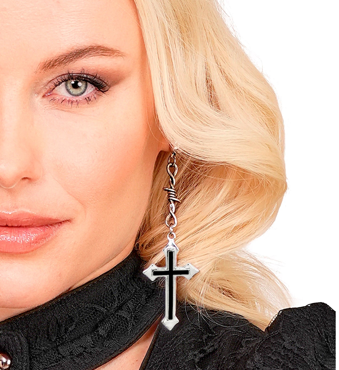 A close-up of a woman with blonde hair wearing a gothic cross and barbed wire earring.
