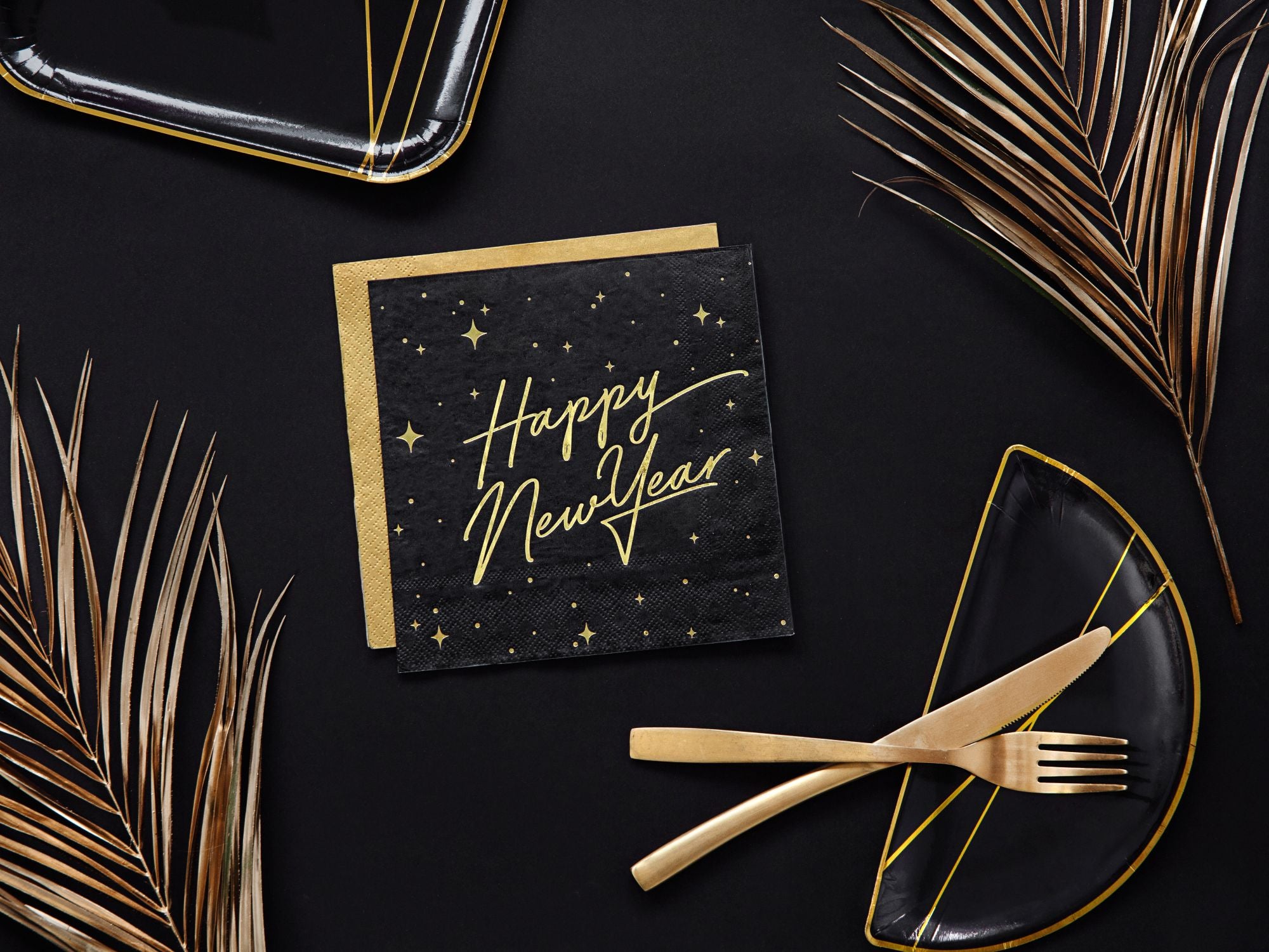 Elegant New Year’s Eve table setting with black and gold napkins and gold silverware.