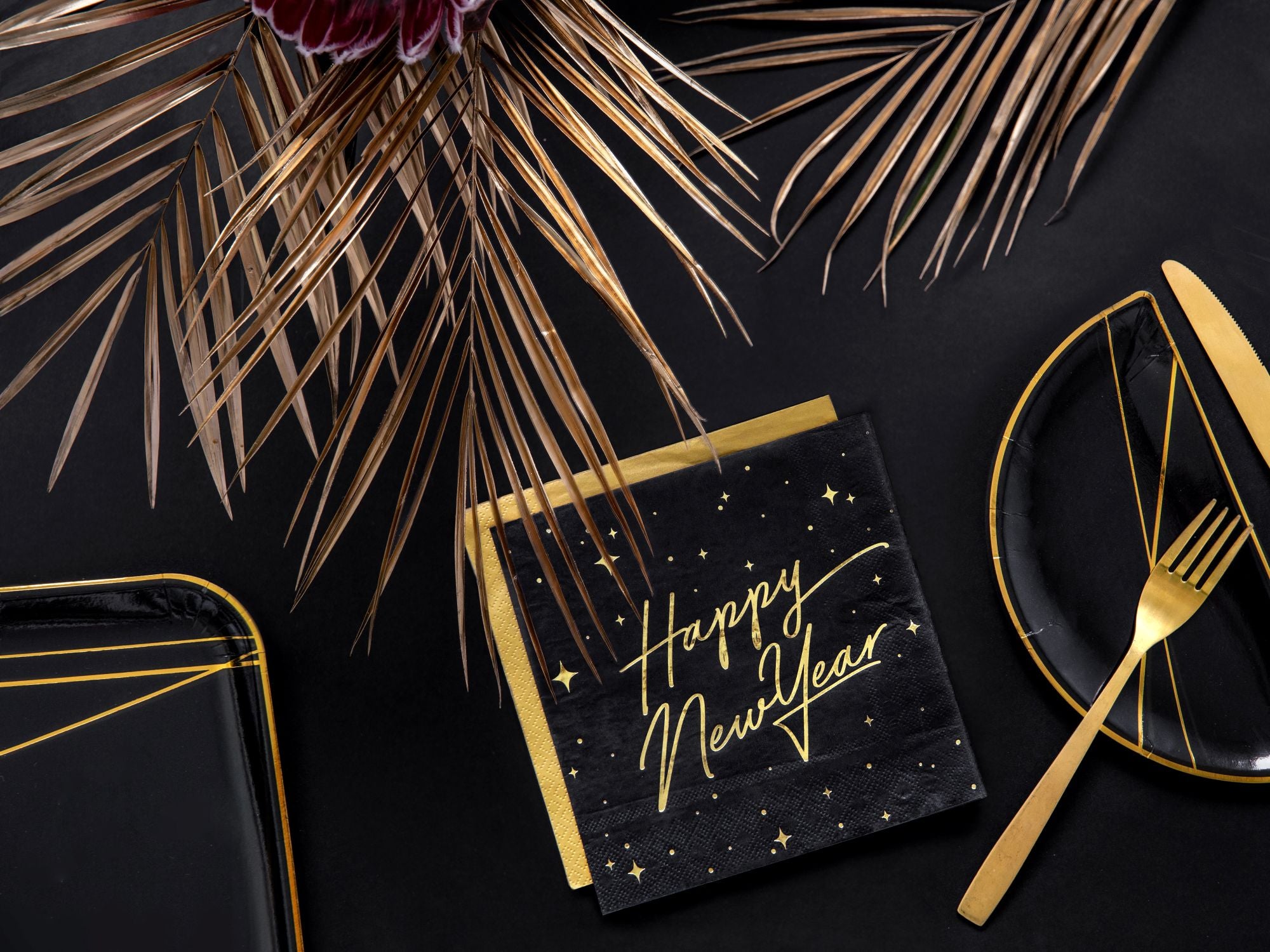 Black and gold 'Happy New Year' card on a dark surface with decorative leaves and cutlery.